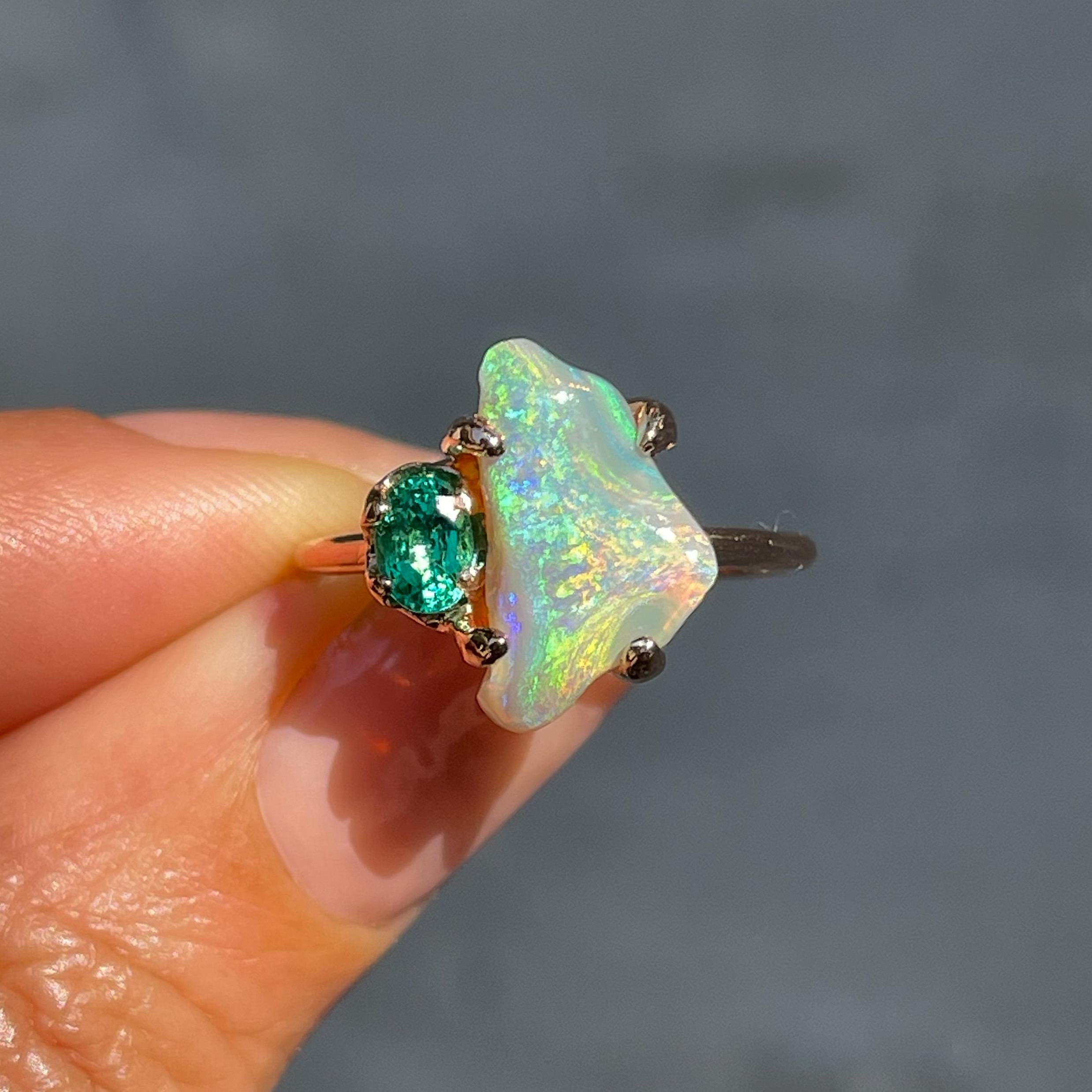Der Schwarze Opal in diesem Ring aus Opal und Smaragd besticht durch seine geschmeidige, blühende Farbe. Der Lightning Ridge Opal ist mit einem ovalen Smaragd in Roségold gefasst und strahlt ein Ethos der Erneuerung aus. Der chromatische Fluss