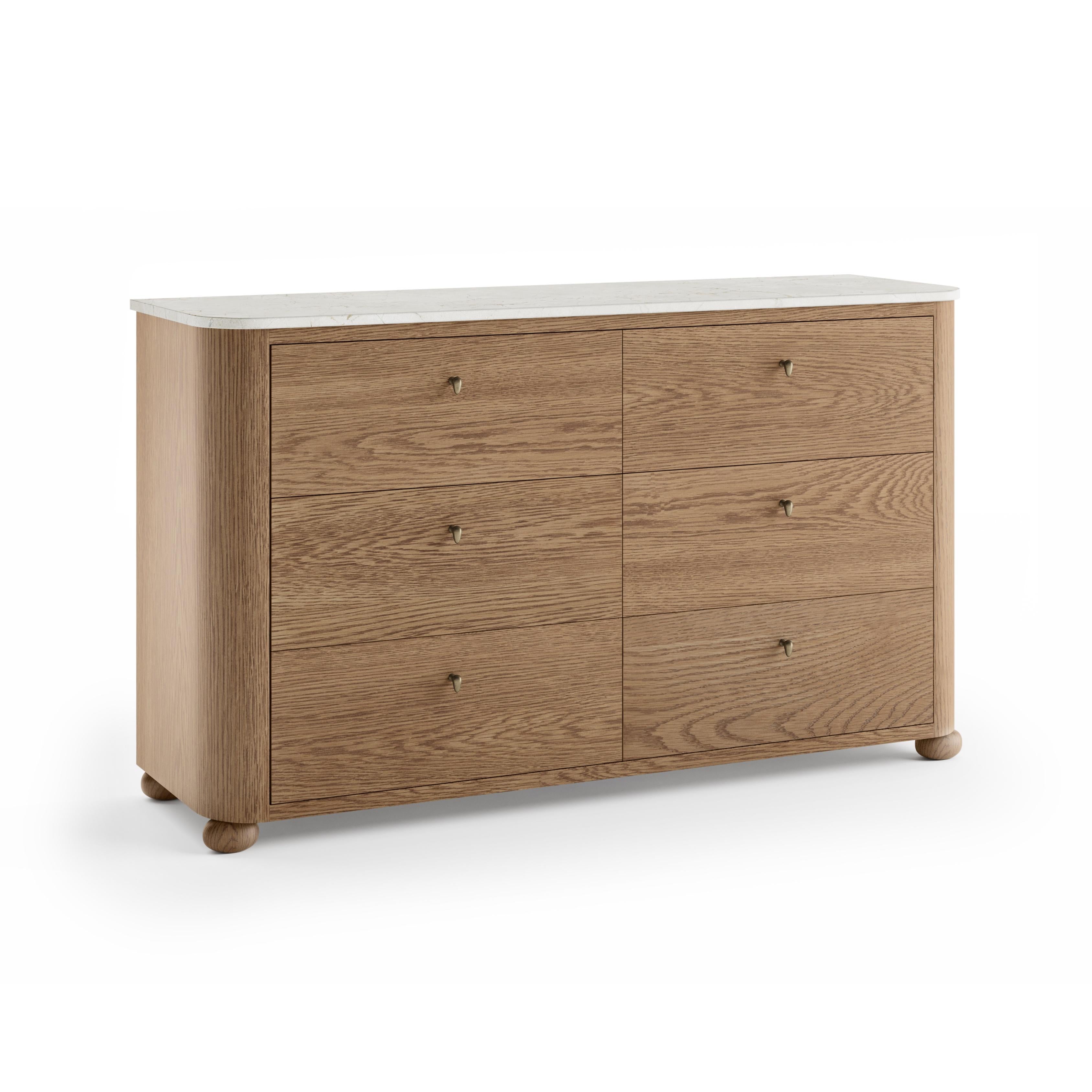 A honed marble top sets a refined tone, while bronze hardware invites a subtle touch of warmth. The form is understated yet striking—solid wood in a minimalist silhouette, balanced on gently rounded feet. The dresser features six soft-close