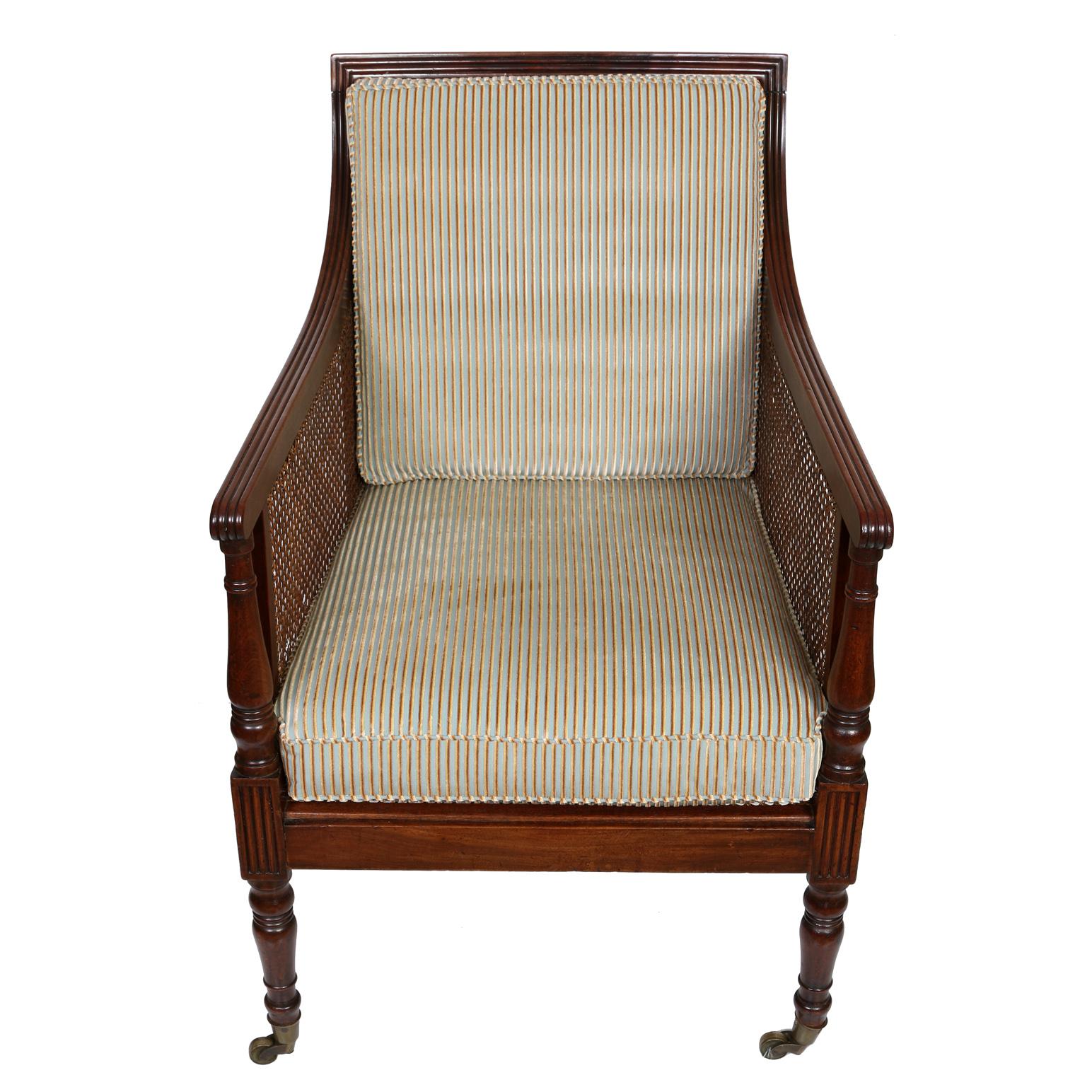 An almost pair of Regency style library chairs with distinctive caning to back, seat and sides with fluted frame and caster wheels.  Both handsome wood chairs have newly upholstered striped velvet fabric to back and seat cushions, with one chair