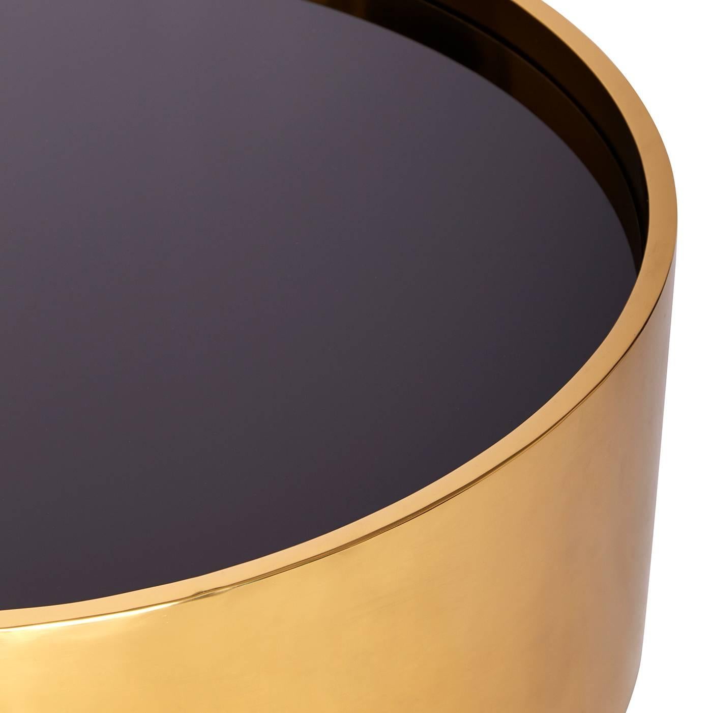 Riflessione futuristica. Minimalista e moderno, il nostro tavolo da cocktail Alphaville risplende in ottone lucido con un piano in vetro nero. La semplice forma a tamburo è una solida ancora per qualsiasi stanza, mentre la superficie riflettente