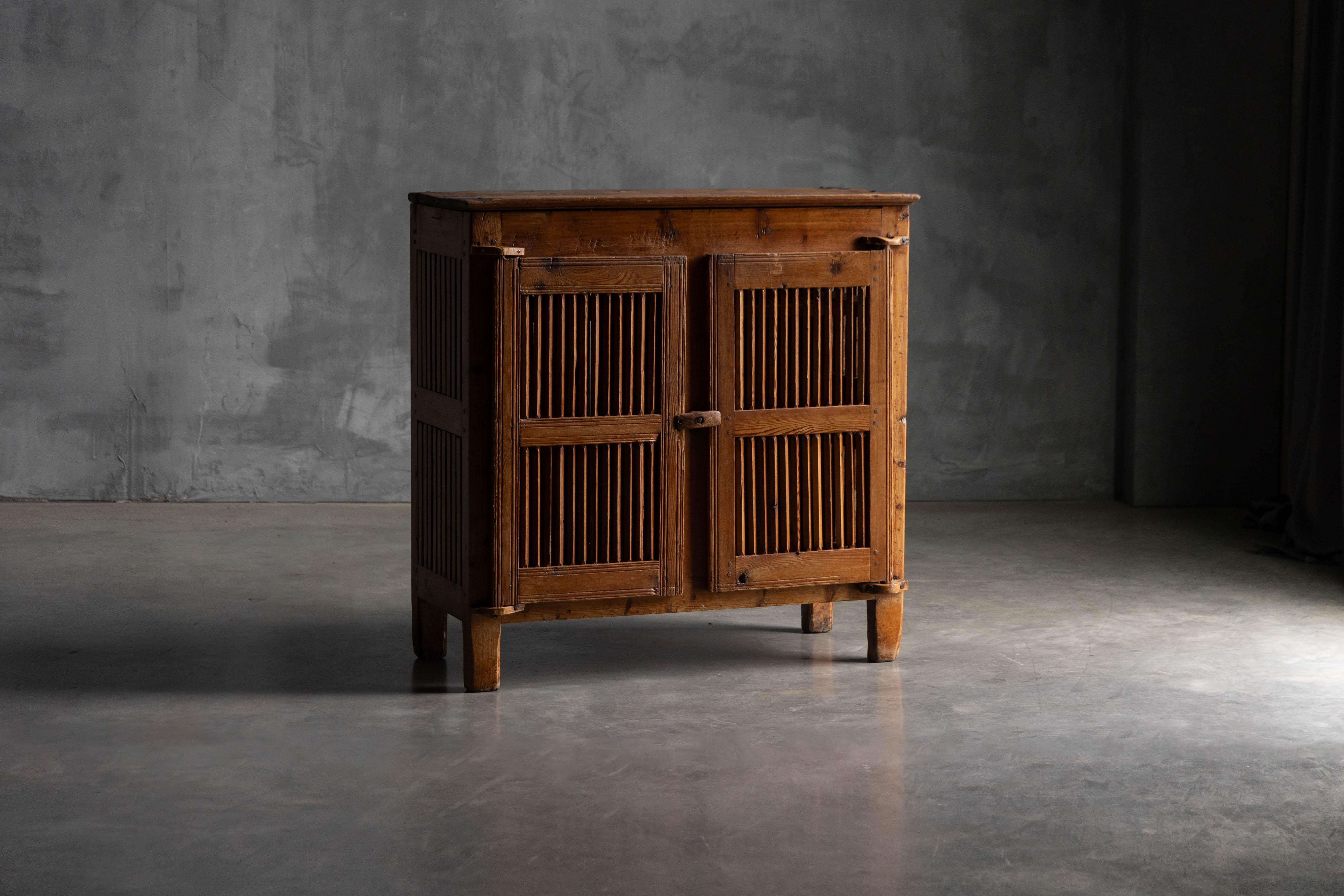 This antique wooden cabinet is a traditional tommière from Champcella in the French Alps, crafted in the 19th century for drying and storing cheese. Made entirely of pine with slatted doors and sides, it features wooden pivot hinges and a rustic