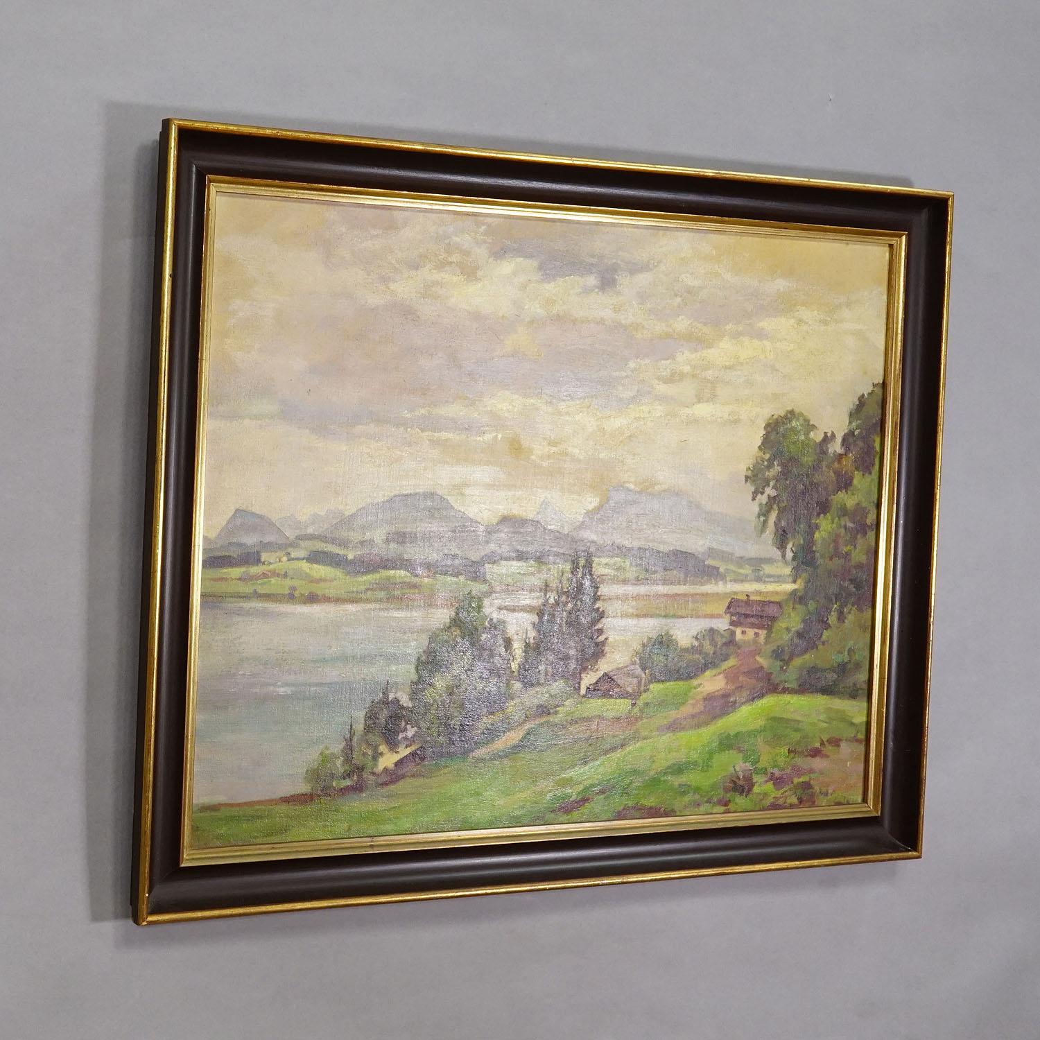 Alpine Lake View Oil Painting with Tyrolean Hut

A large landscape painting in a dark brown frame with a gold inner lining. The scene features a peaceful lakeside view with gently rolling green hills, scattered trees, a small mountain hut, and