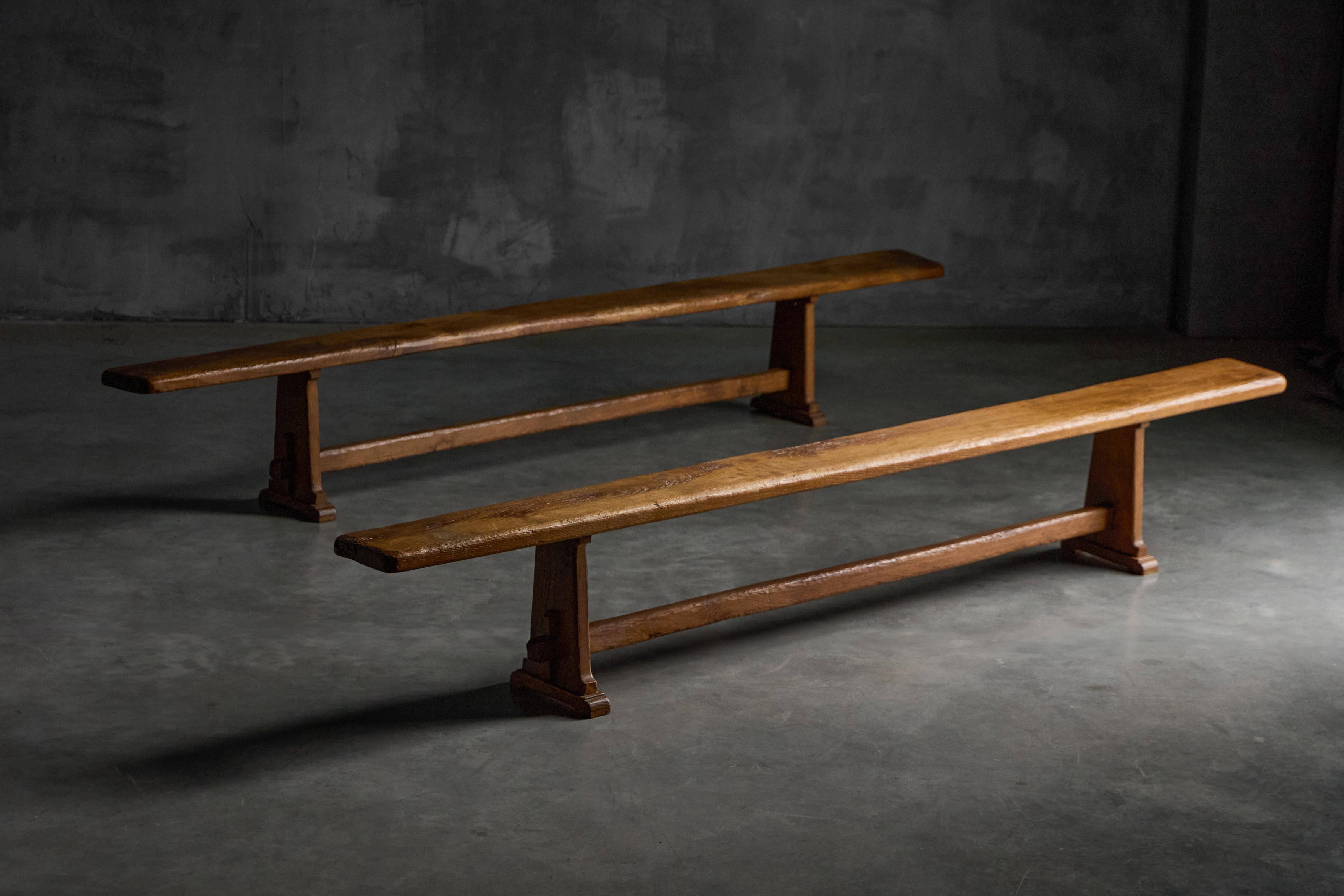 Estos bancos alpinos artesanales de mediados de siglo, hechos de madera maciza con una hermosa pátina envejecida, presentan asientos gruesos y sutilmente curvados sobre robustas patas de estilo caballete. La carpintería es a la vez práctica y