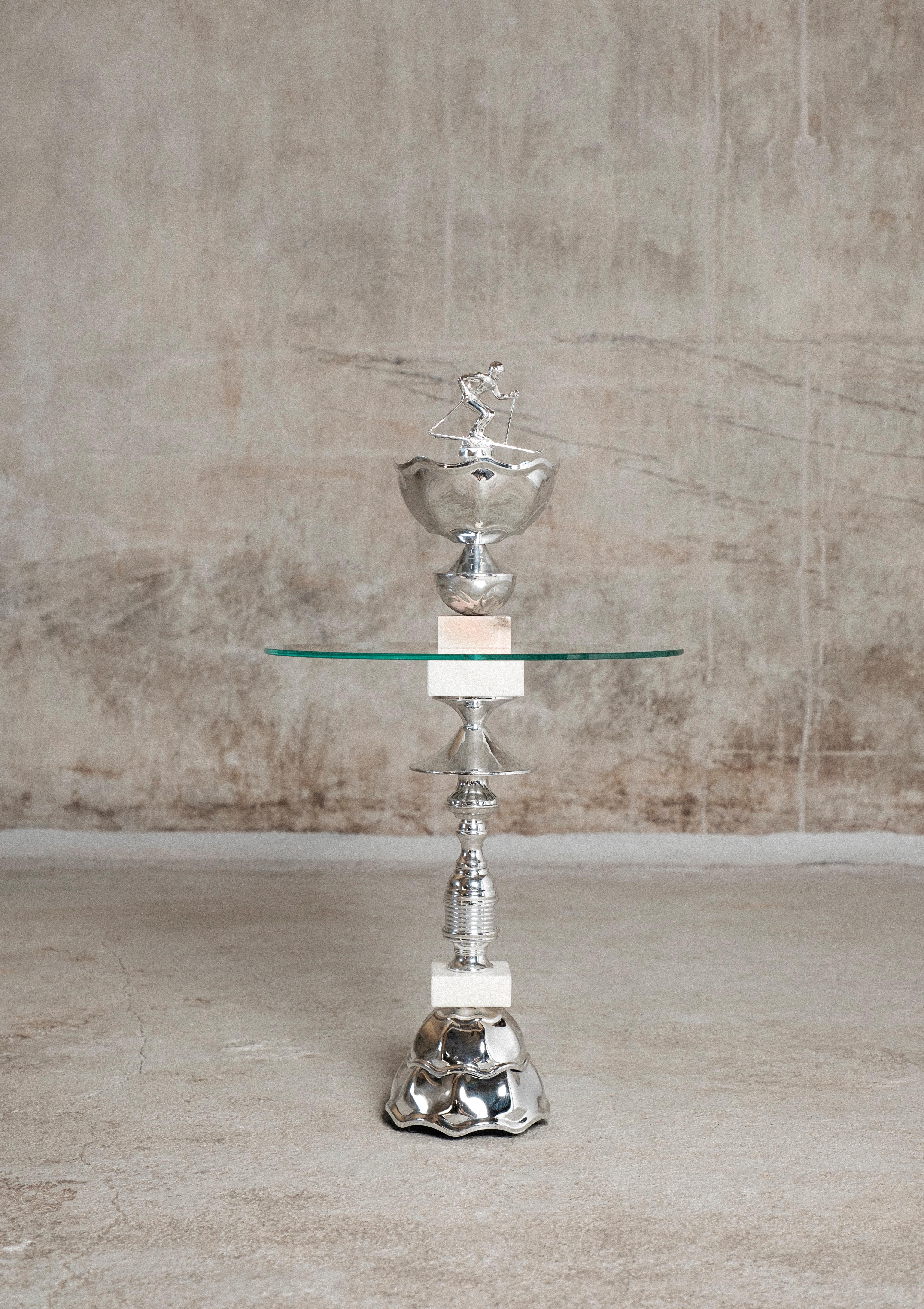 The Alpine Skier table by Flétta
Dimensions: 74 x 46 cm
Materials: silver, white, rose marble

Trophy is a collection of tables, lights, flowerpots and shelves made of old trophies collected from athletes and sports clubs in Iceland. Trophies