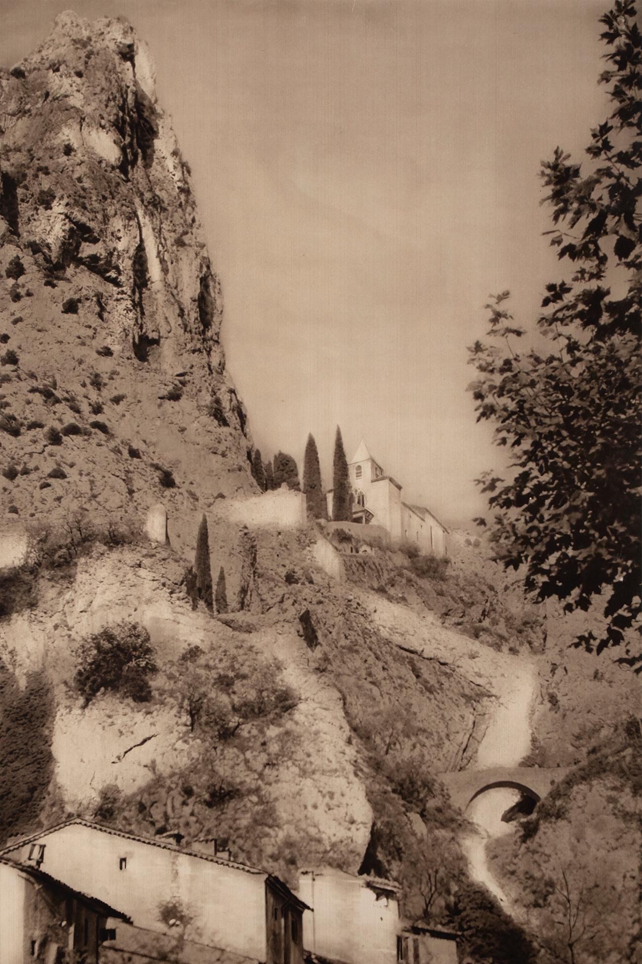 Striking sepia-toned French travel poster featuring the glorious Moustiers-Sainte-Marie in Alpes De Provence.

From a series of posters made to promote regional tourism in France.

In excellent original condition, professionally framed with