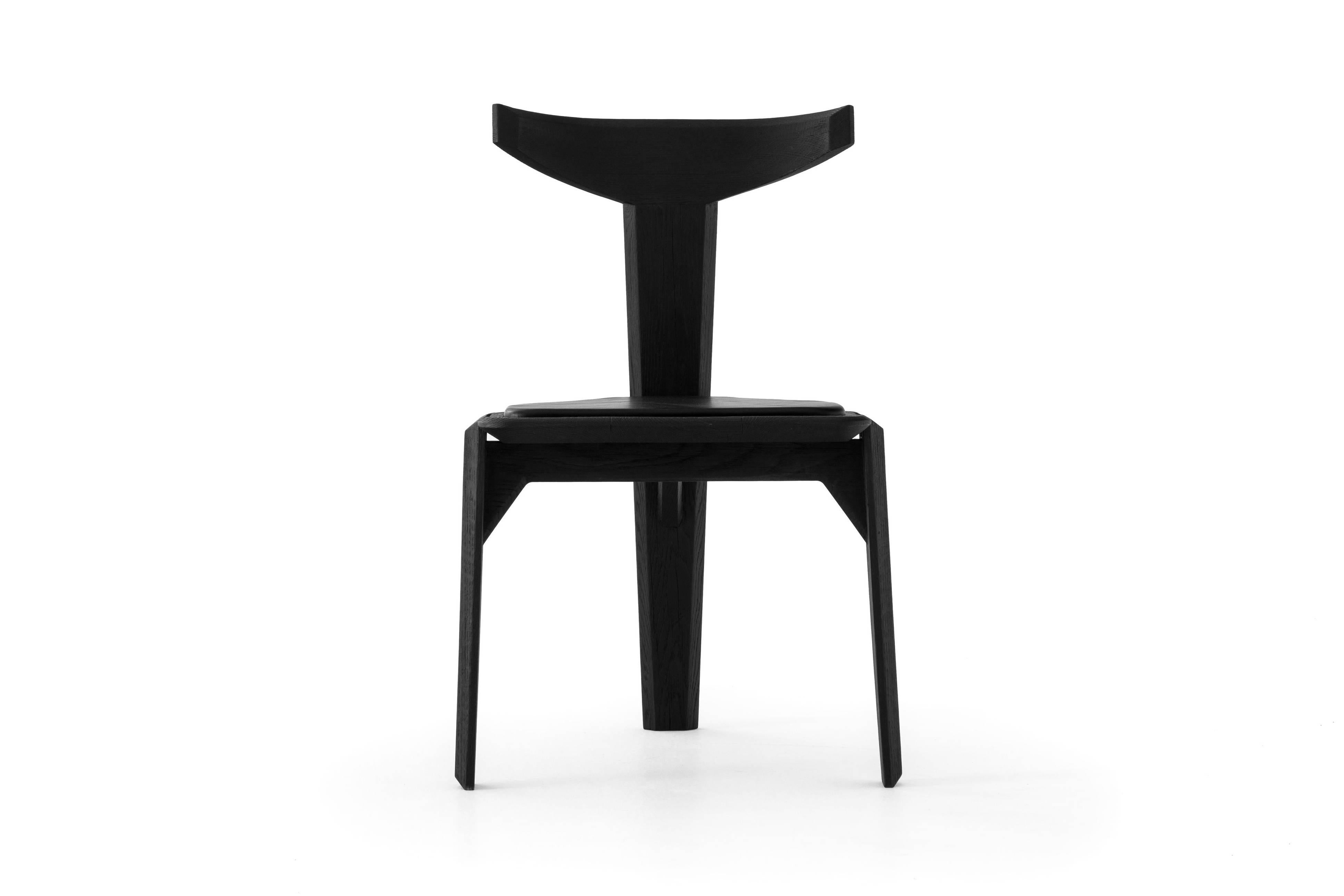 the Ceniza Chair, carved by hand and assembled by a master cabinetmaker, consists of three legs, a leather seat, and an iconic backrest. Its wooden black leather upholstered seat is attached to the three legs using an ancient technique called Espiga