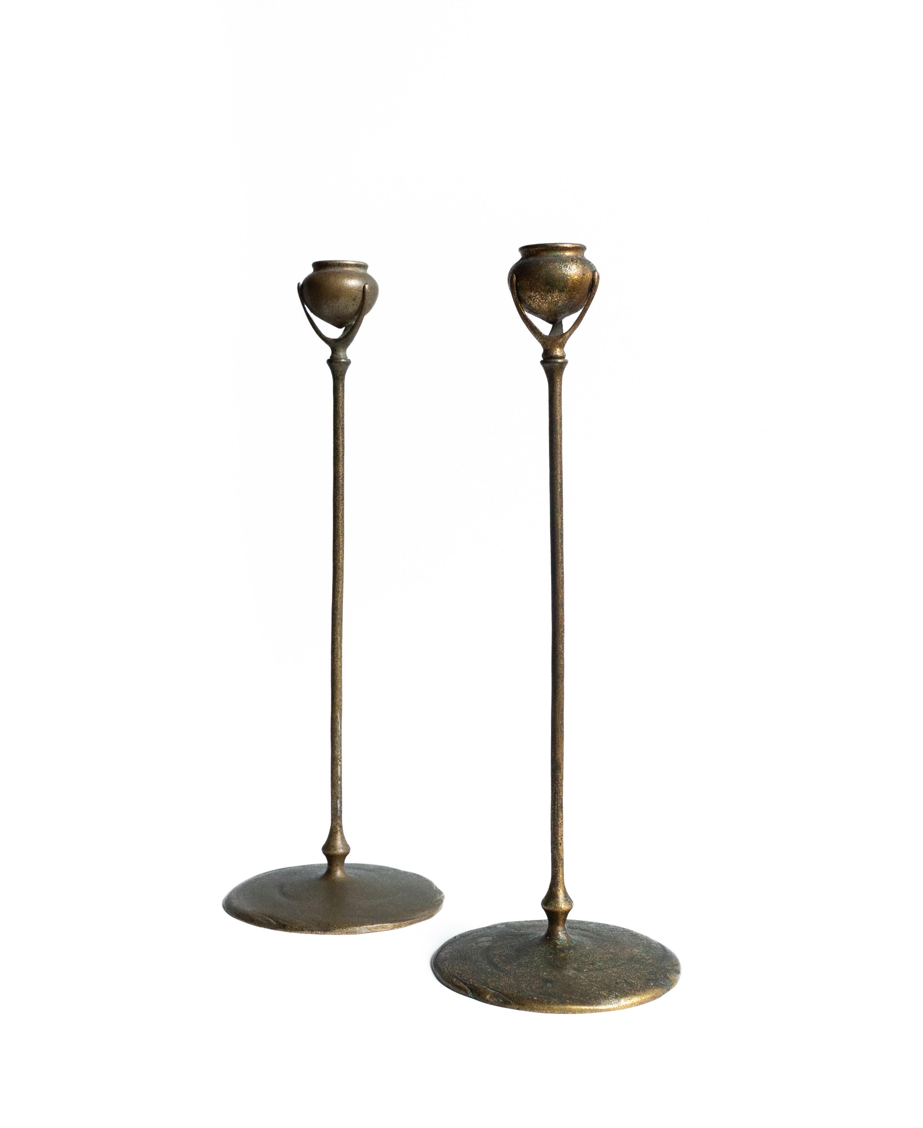 Un par emparejado de art nouveau  Candeleros altos y esbeltos, De bronce patinado oscuro y bronce dorado. 
Un gran disco con borde ondulado y textura arremolinada sirve de pie a la composición, desde el que se extiende hacia arriba un tallo rígido,