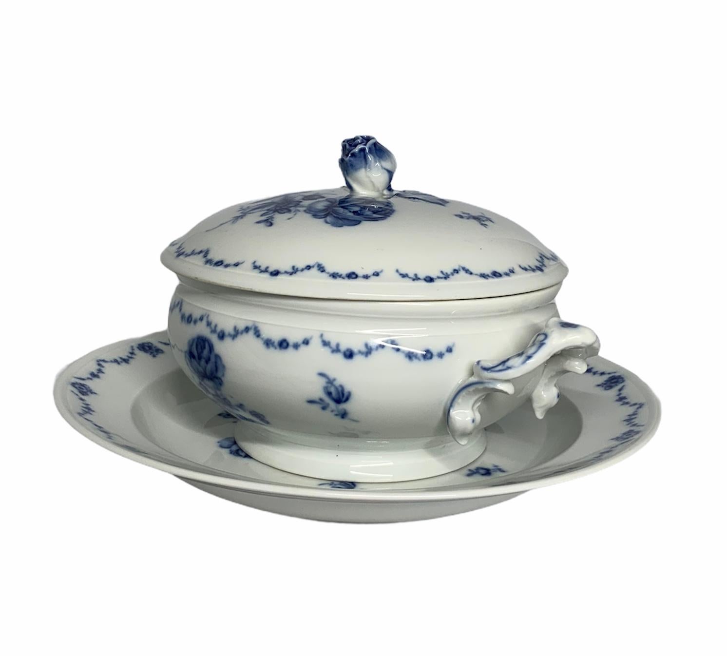 This is an Alt Furstenberg Lottine porcelain white tureen decorated with royal blue roses and foliage. There are garlands with this pattern adorning the borders of the lid, the bowl and the plate. The tureen has scrolls handles at each side