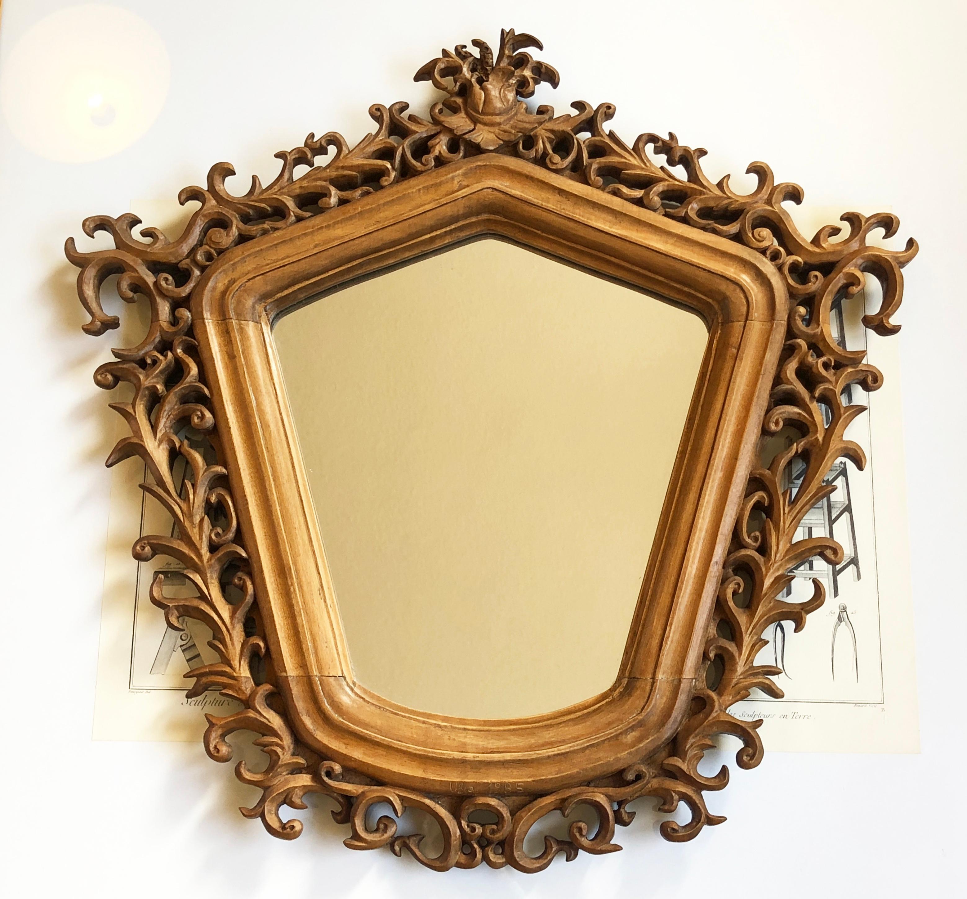 Wonderful rarity: mirror in a unique shape, handmade most likely in Italy.
Baroque or Rococo style, magnificent carving with slightly chivalrous symbolism at the top. 
Roughly notched year & name below: Ubro (Usro?) 1985. 
This will have been added