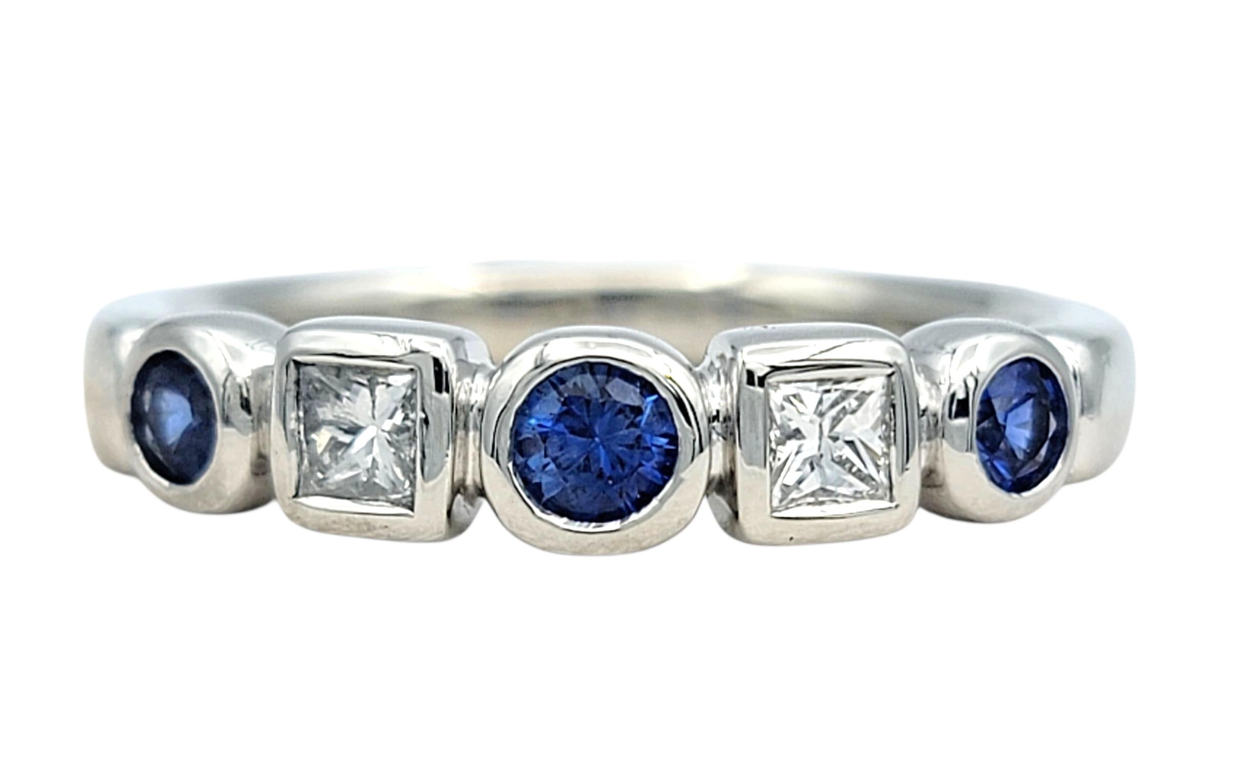 Dieser elegante Ring aus Platin zeigt eine harmonische Anordnung von funkelnden Diamanten und blauen Saphiren in einer Lünettenfassung. Zwei Diamanten im Prinzessinnenschliff sind zwischen drei natürlichen blauen Saphiren im Rundschliff platziert