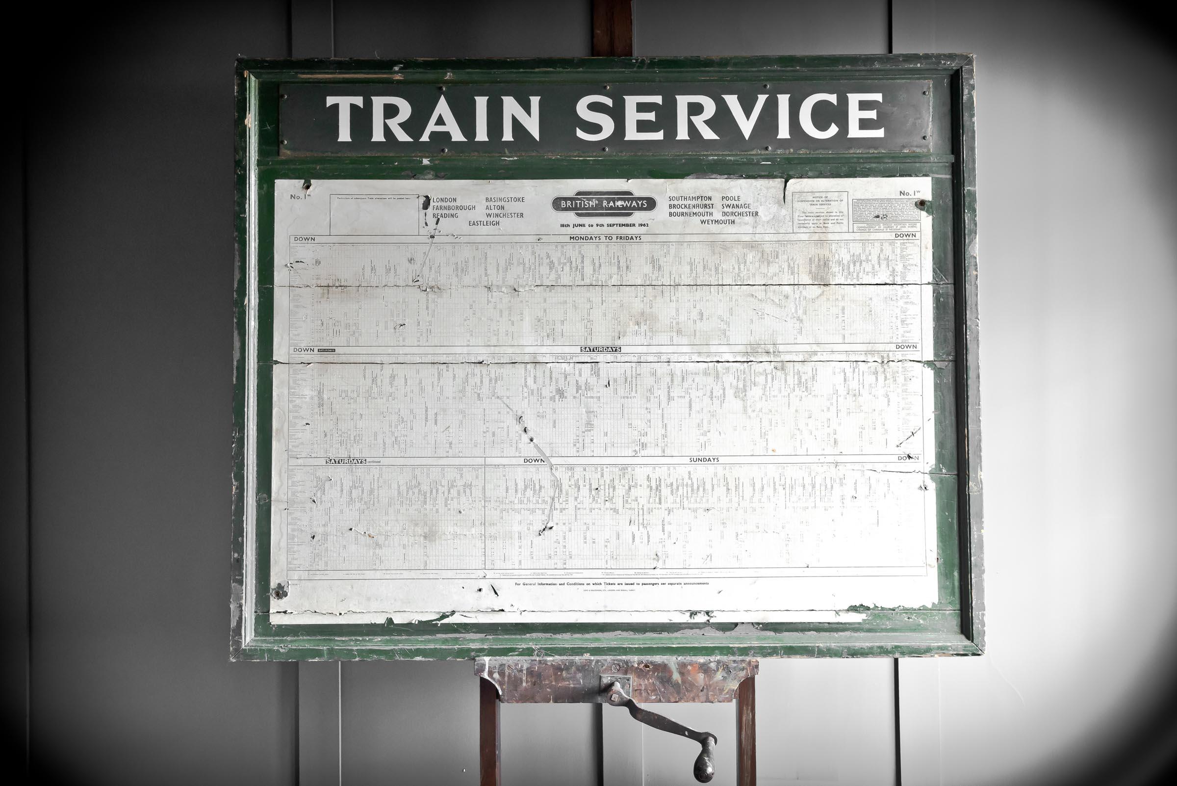 Train service timetable sign originally from Alton train station for the year 1962. Paper timetable mounted on a wooden green frame.