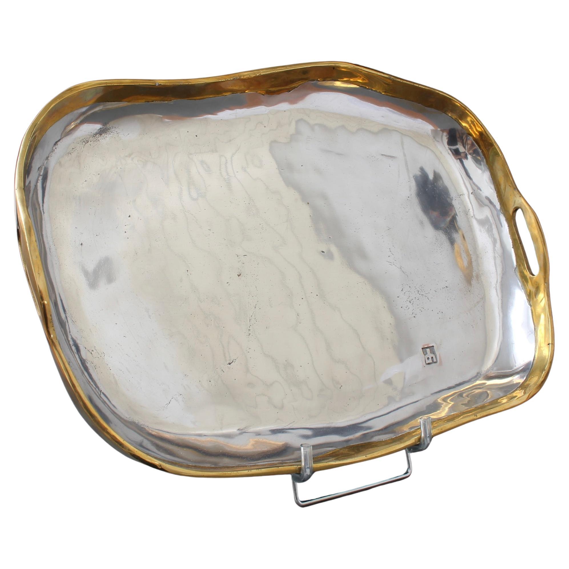 Gran bandeja de aluminio y latón de estilo brutalista, obra de David Marshall (hacia la década de 1980). El aluminio brillante forma la estructura principal y las asas de latón están en ambos extremos. La marca del fabricante está impresa en la
