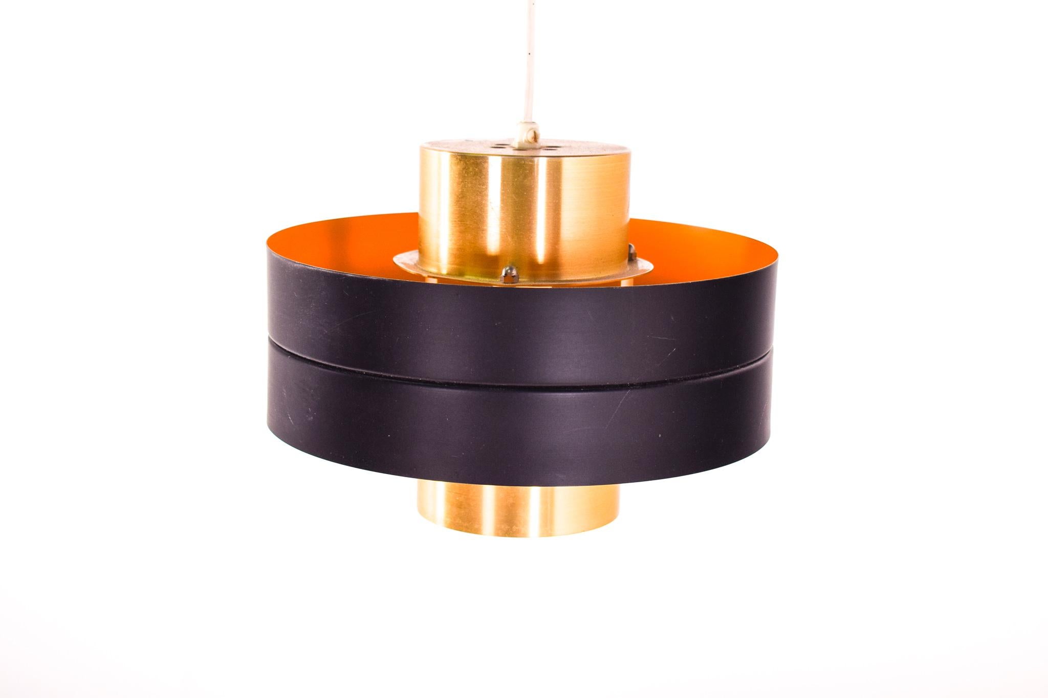 The lamp consists of two aluminium lacquered in brass shades with a black band that runs around the middle. The interior is painted on yellow, which gives it a warm color when switched on. This Danish pendant lamp very reminiscent to those lamps