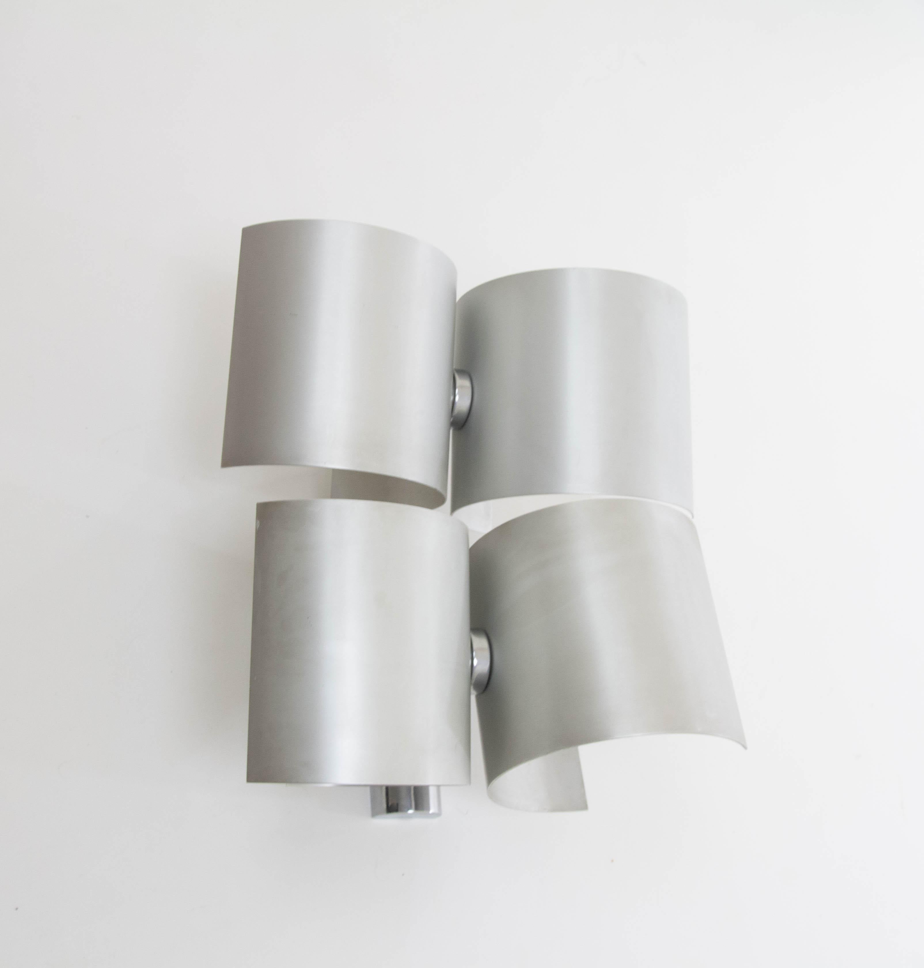 Wall lamp produced by Nucleo Sormani in the 1970s.

The lamp consists of four -similar but not the same- curved aluminum parts, each with a light bulb socket (E14). Each part can rotate independently of the other parts, thus offering a wide range of
