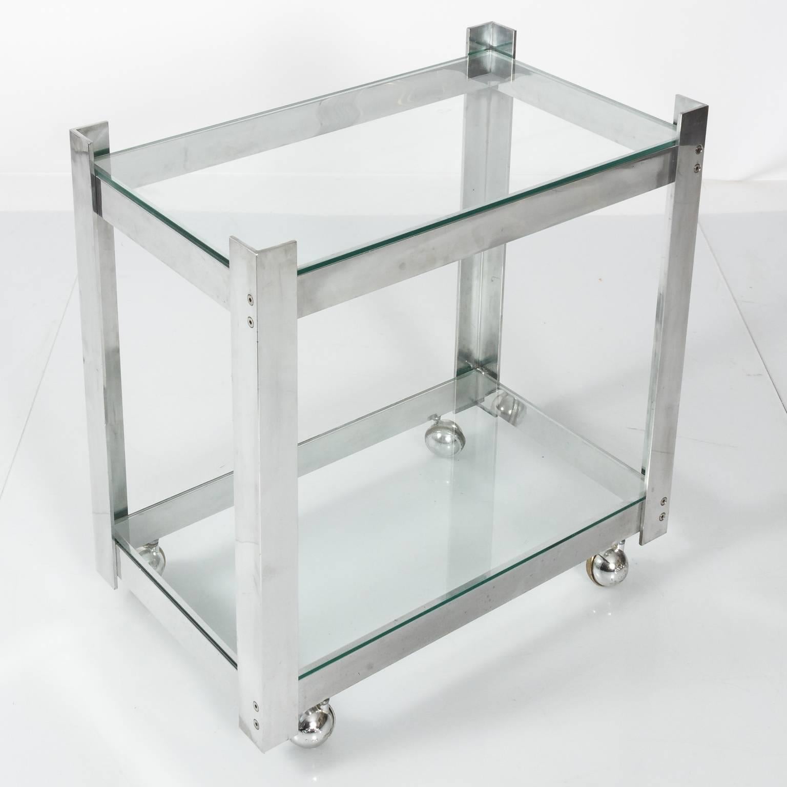 Two-tiered aluminum bar cart with glass shelves on wheels in a polished finish.
 