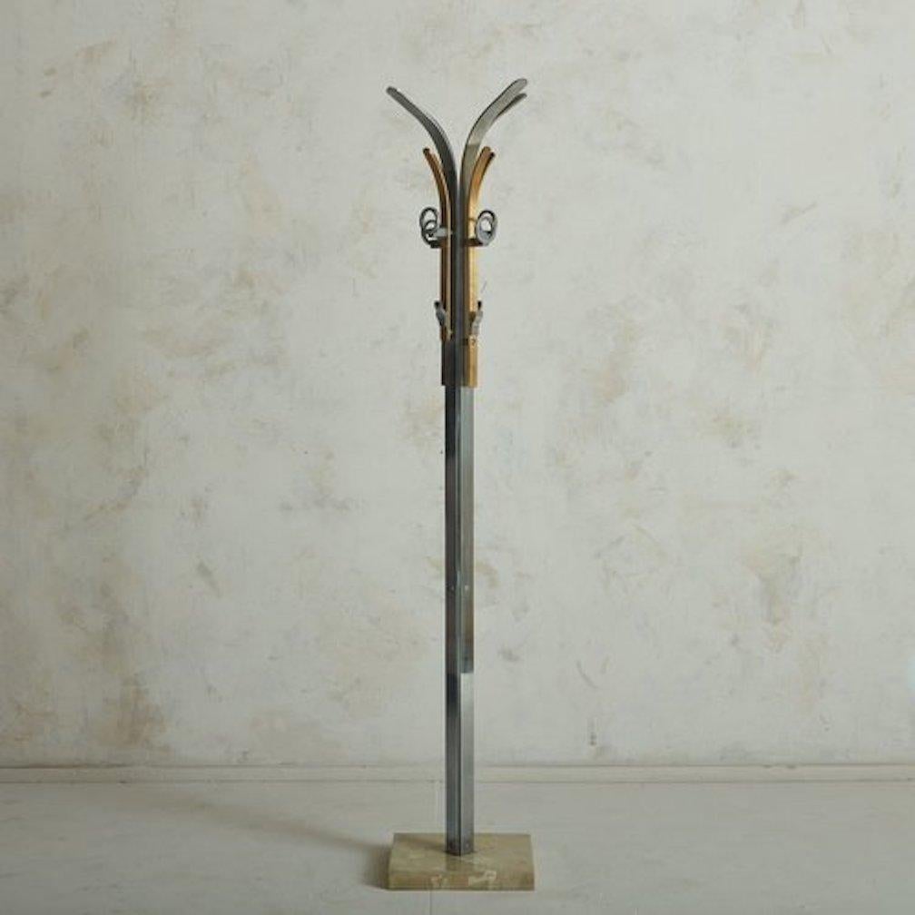 A vintage Italian coat rack featuring a sculptural aluminum frame with brass detailing. This piece has four circular hooks and four additional hooks for coats, hats or accessories. It has a square cream marble base with beautiful salmon and gray
