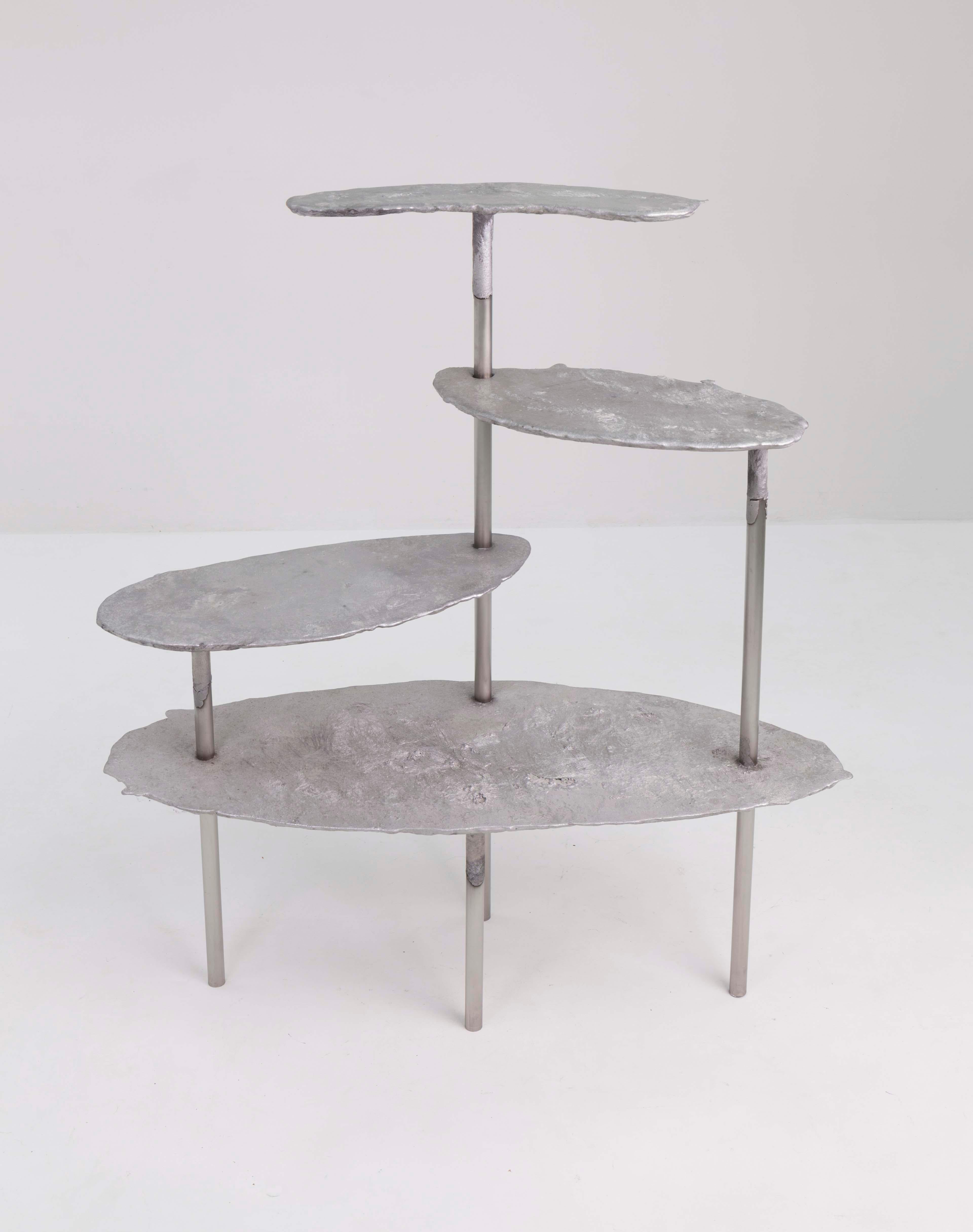 Aluminum concretion shelf by Studio Julien Manaira.
Dimensions: 123 x 47 x 141 cm.
Materials: aluminium and stainless steel.

The concretion project consists of sand-casting aluminium in a base of stainless steel tubes to form objects. The tubes
