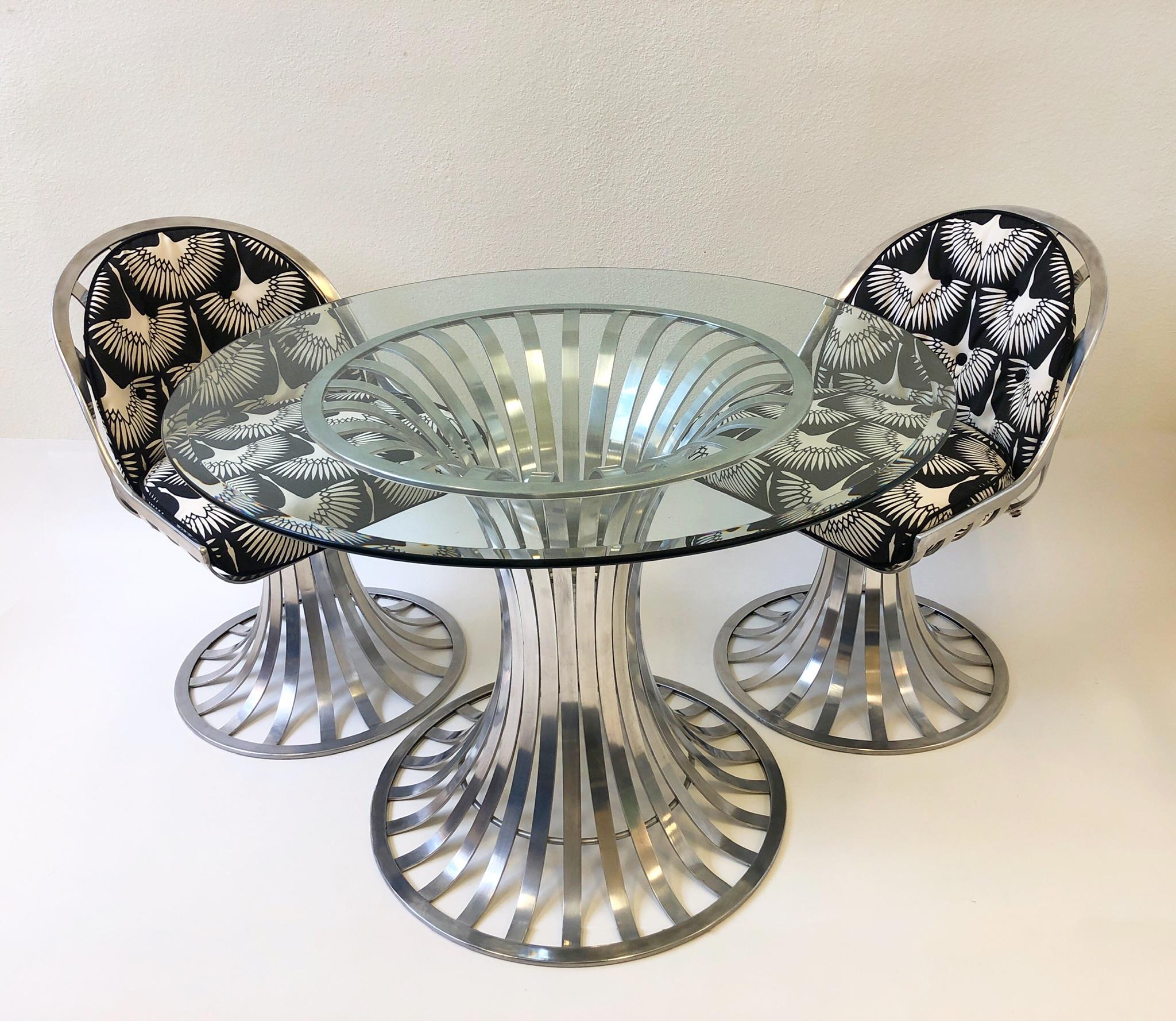 Aluminum patio set designed by Russell Woodard. The set consists of four swivel chairs newly recovered in a Sunbrella fabric with flying cranes designed. The table has a new 48” diameter 1/2” thick glass top. The frames are in original condition, so