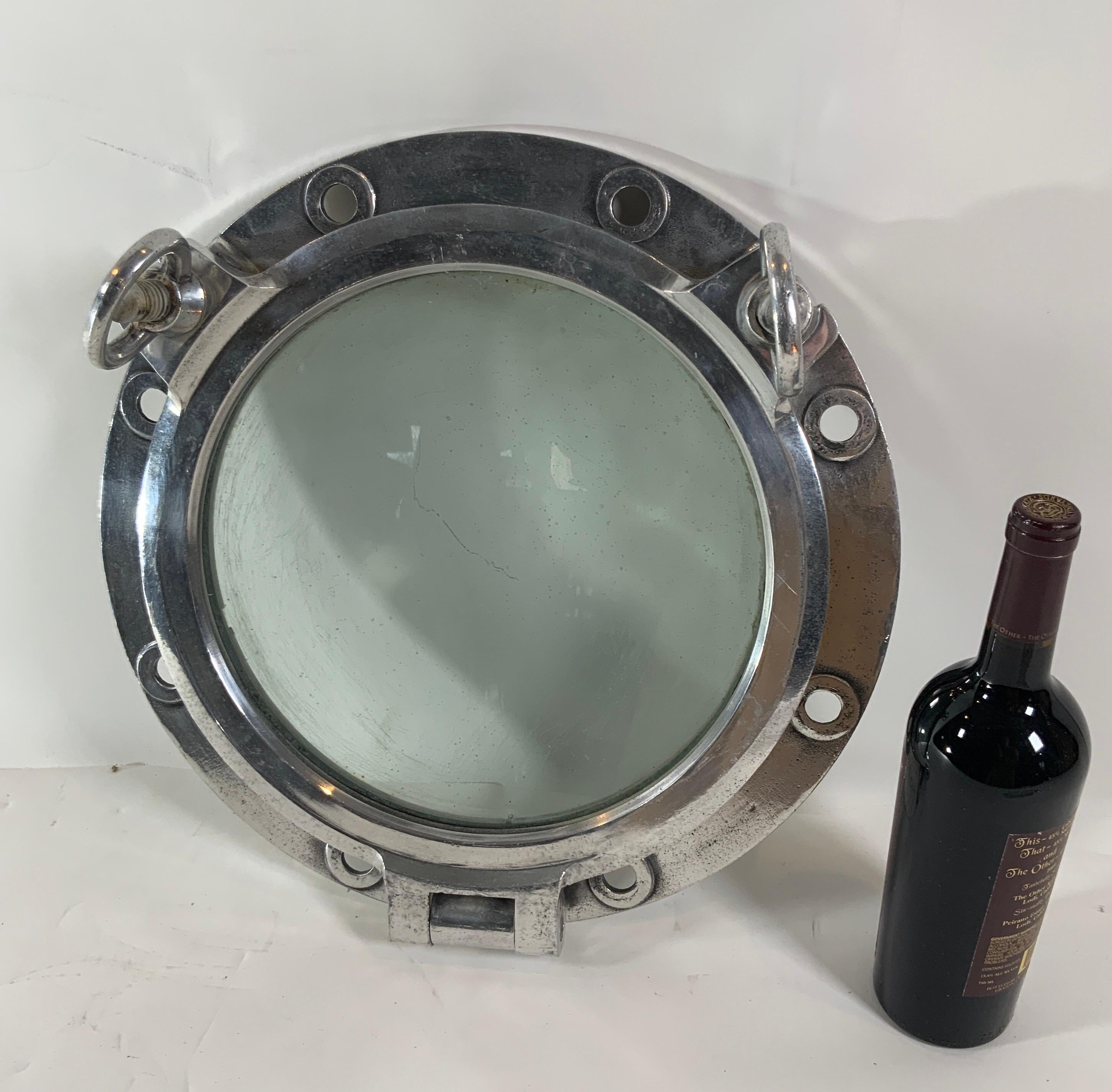 Authentic polished aluminum ship's porthole fitted with a glass window. Door is hinged and fitted with two dogbolts. Highly polished porthole. 

Overall dimensions: glass diameter: 12