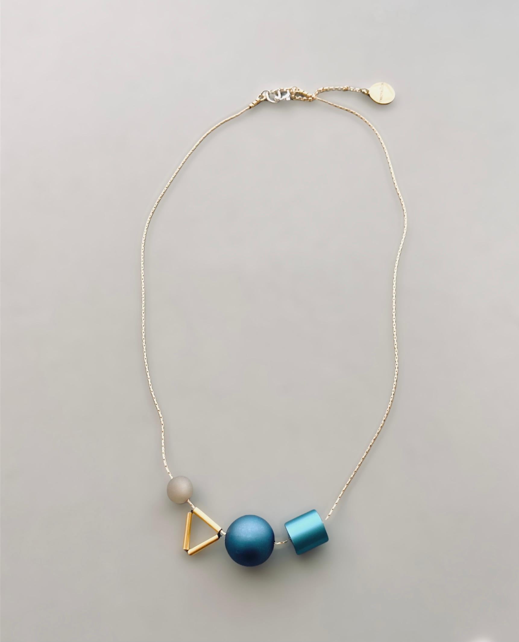 This satin finished aluminum necklace is a favorite among museums.  Very light weight, eye catching and artistic, the Aluminum Triangle necklace is made with aluminum and resin beads.  To add dimension and craft, a triangle group of brass beads is
