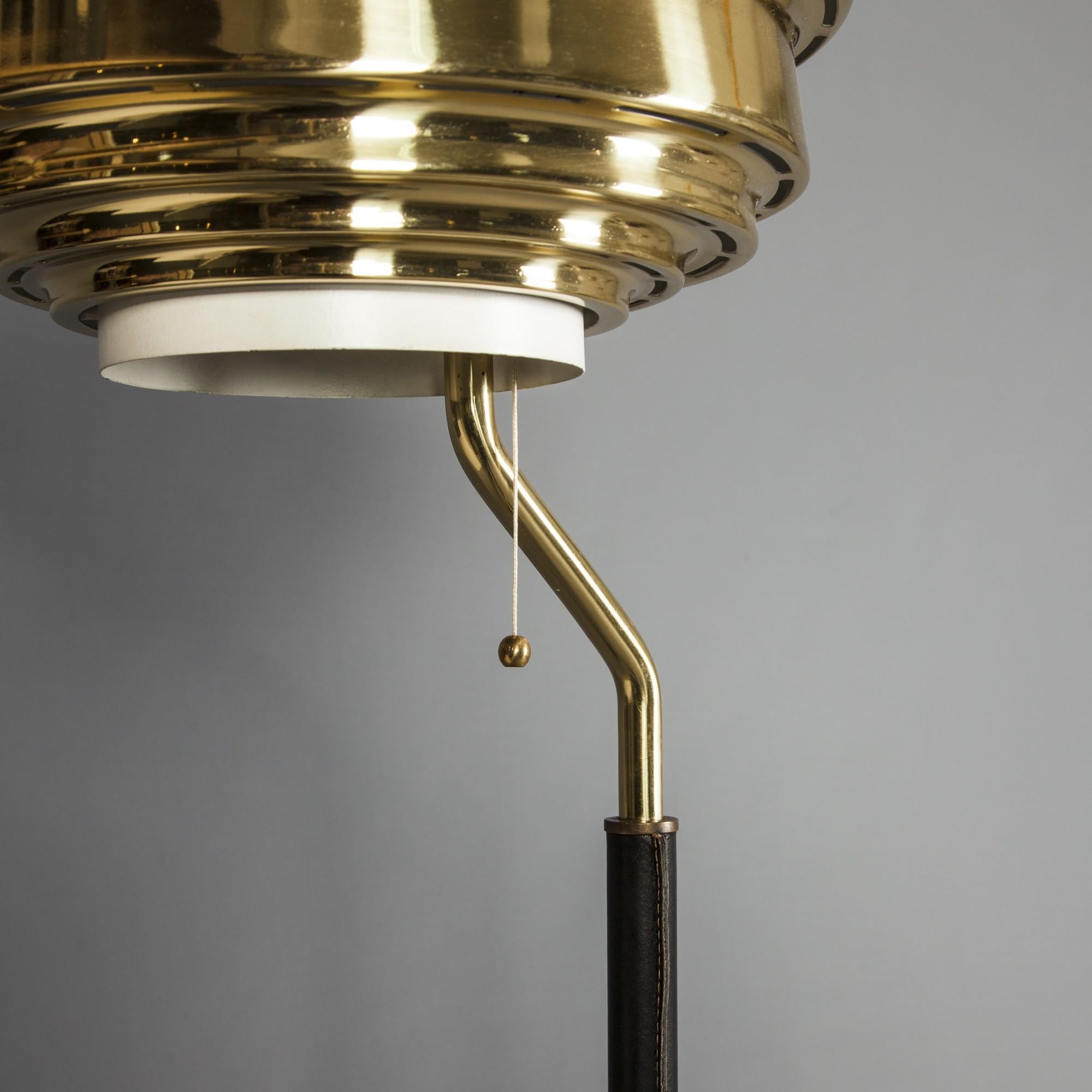 An Alvar Alto floor lamp edited by Valaitustyo Ky in the early 1950s. Brass shade, white metal; black leather-covered lamp stand. Early edition. Top impressed with 