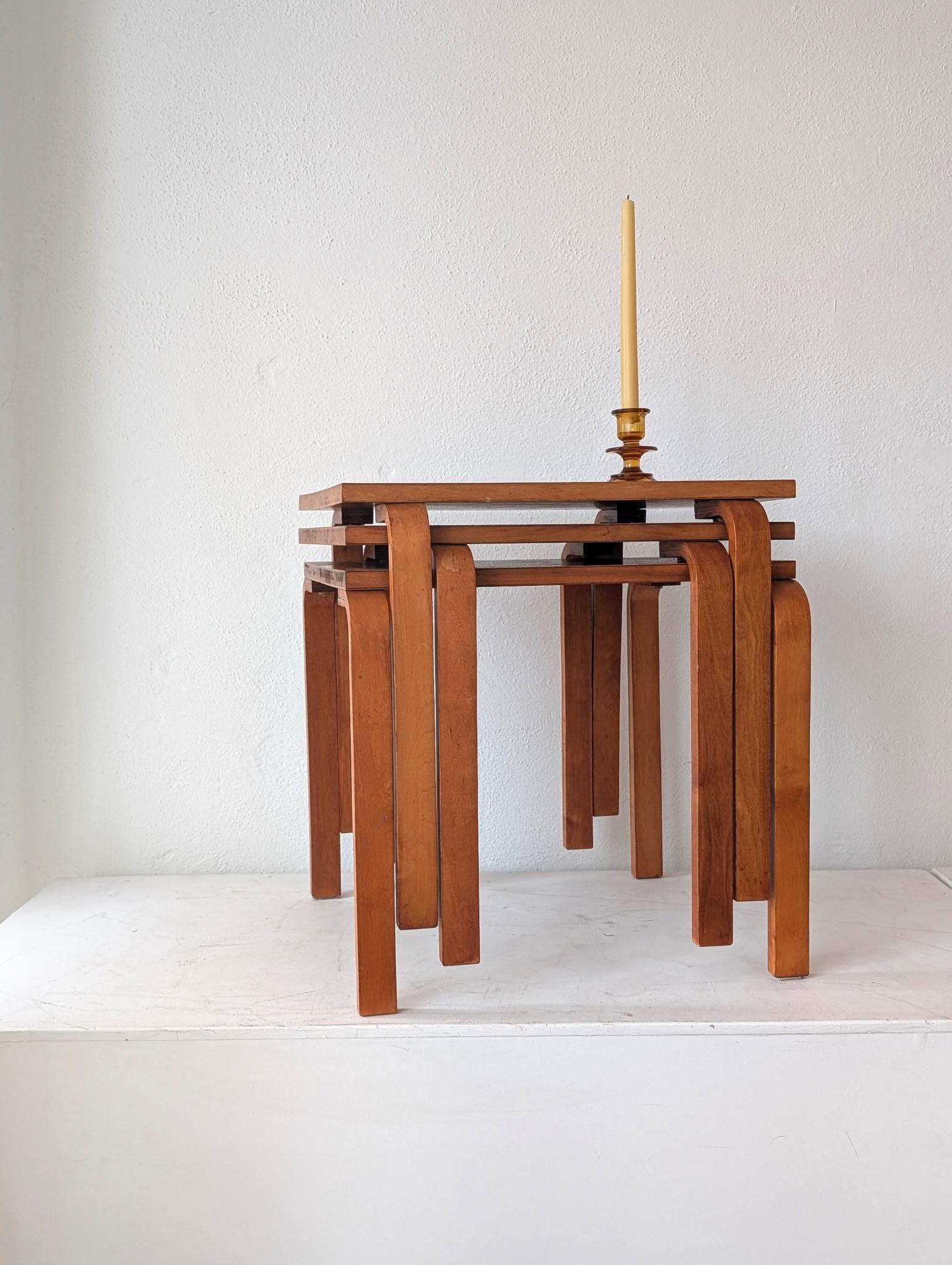Un set di tre tavolini impilabili di Alvar Aalto, raramente trovato intatto, in una splendida tonalità di compensato tinto teak. Ogni tavolo di questo set di tre ha dimensioni identiche rispetto ad altre edizioni e variazioni dei disegni di