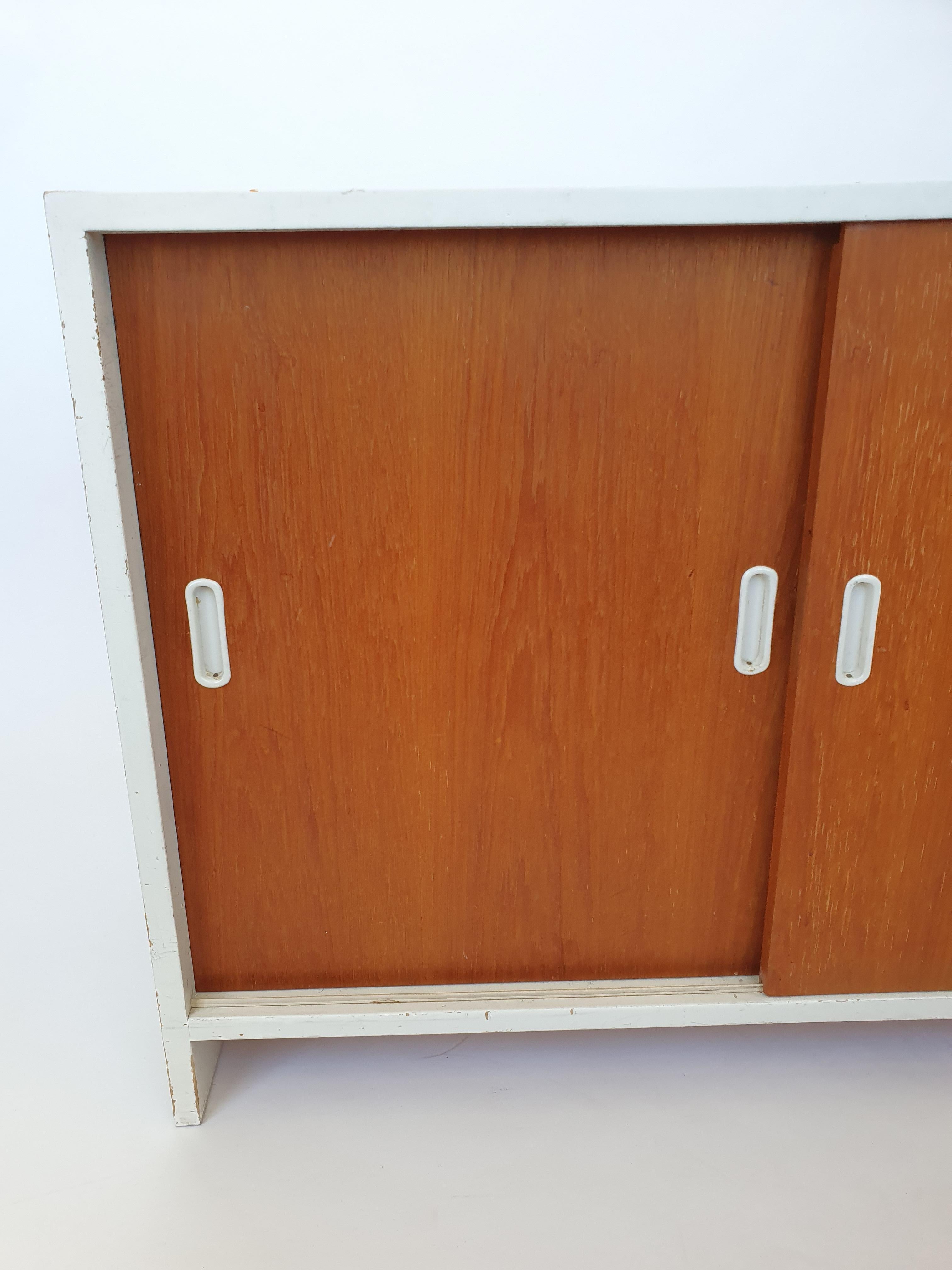 Armadio Artek 217, bianco con ante in teak. In ottime condizioni. L'armadio risale agli anni '60. Il mobile ha 3 ripiani incassati originali con incastri a pettine e 3 ripiani regolari originali. Timbro Artek sbiadito sul retro del mobile.

Il