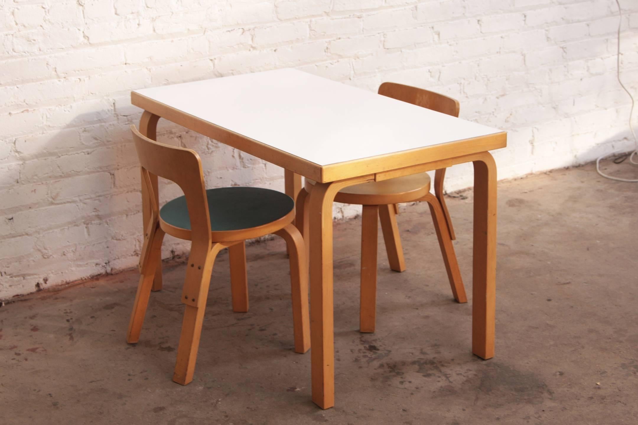 Table and two chairs designed by Alvar Aalto for a child for Artek Finland. His classic bent plywood set. White laminate table top on birchwood. Children's seats are blue and yellow.

Table size: 23.5