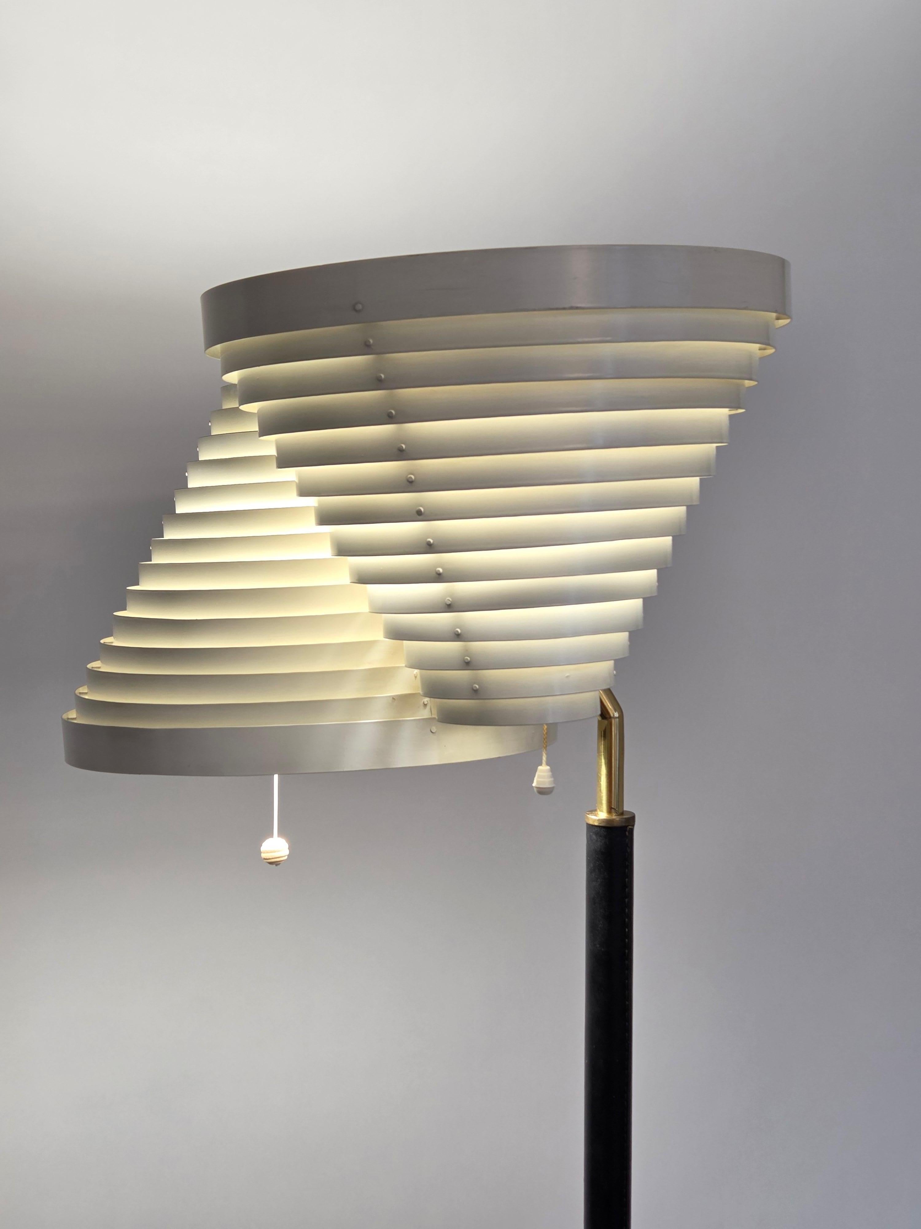 Early Artek A809 floor lamp, manufactured by Valaistustyö, designed by Alvar Aalto in 1959. The lamp has a brass base, black leather, and a white metal shade. The lamp is in good used condition for its age. This lamp is from around 1960s.

