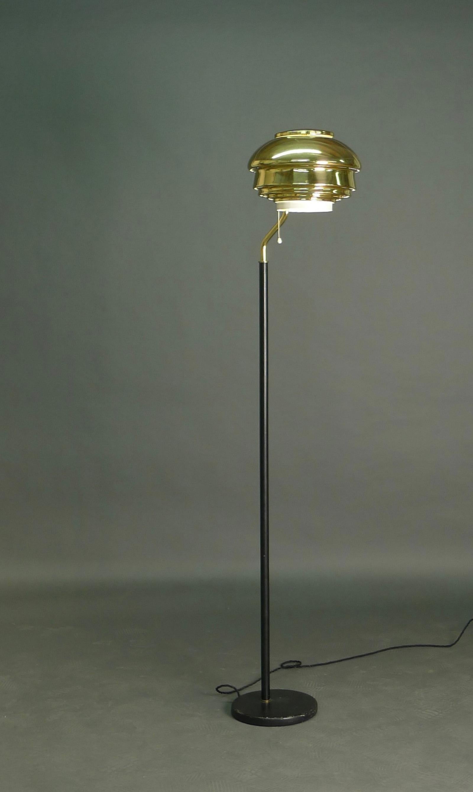Early floor lamp, model A808, designed by Alvar Aalto and manufactured by Valaistustyö, Finland 1950s.  

The layered brass shade with internal white enamelled metal diffuser and pull cord, extended on a brass arm and black leather covered column