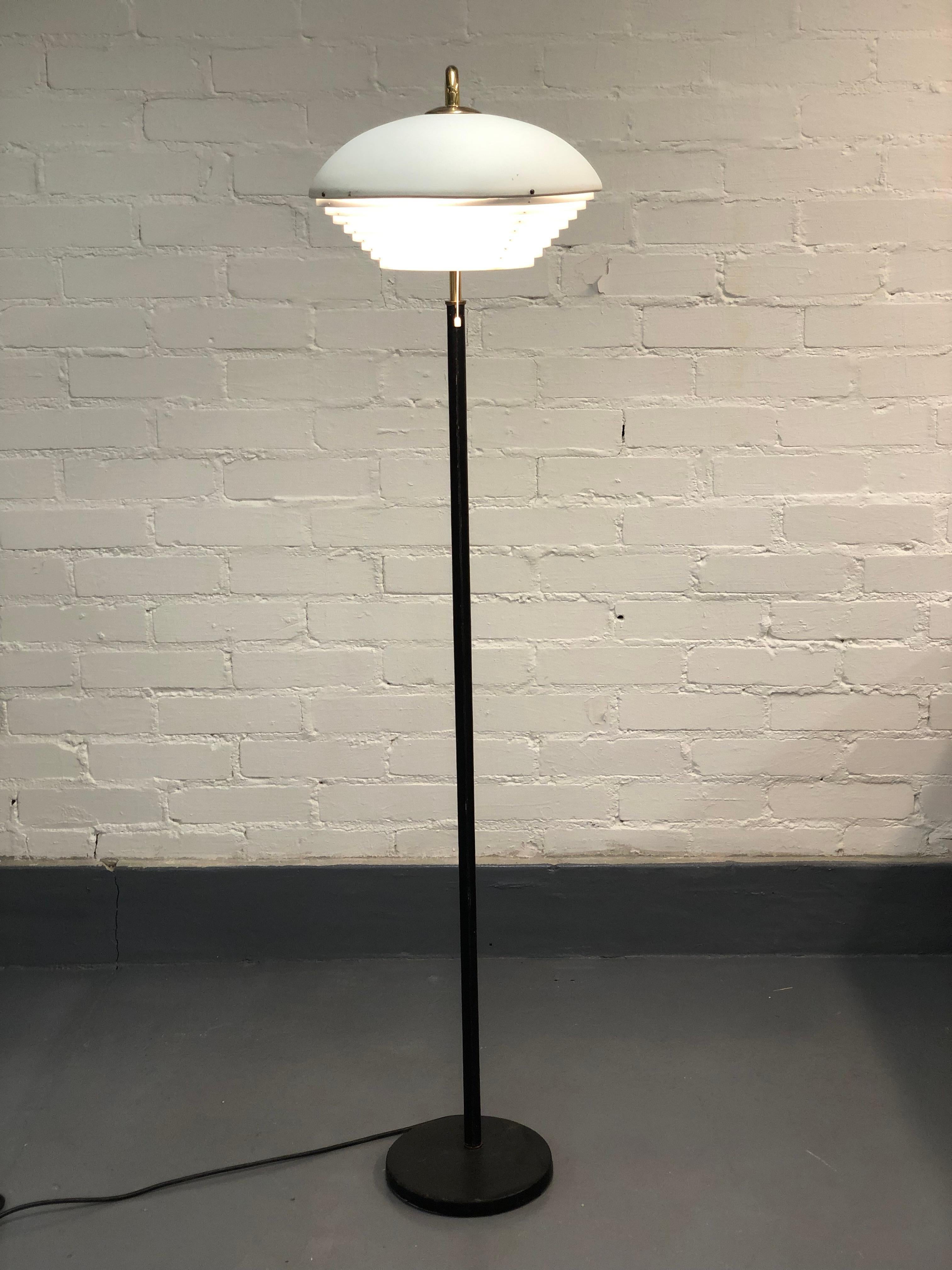 Diese ikonische Stehlampe von Alvar Aalto hat einen Schaft aus Leder, Messingdetails und ein weißes Metallnest auf der Spitze. Der Glanz dieser Lampe liegt in der Einfachheit und der Art und Weise, wie all diese verschiedenen Materialien