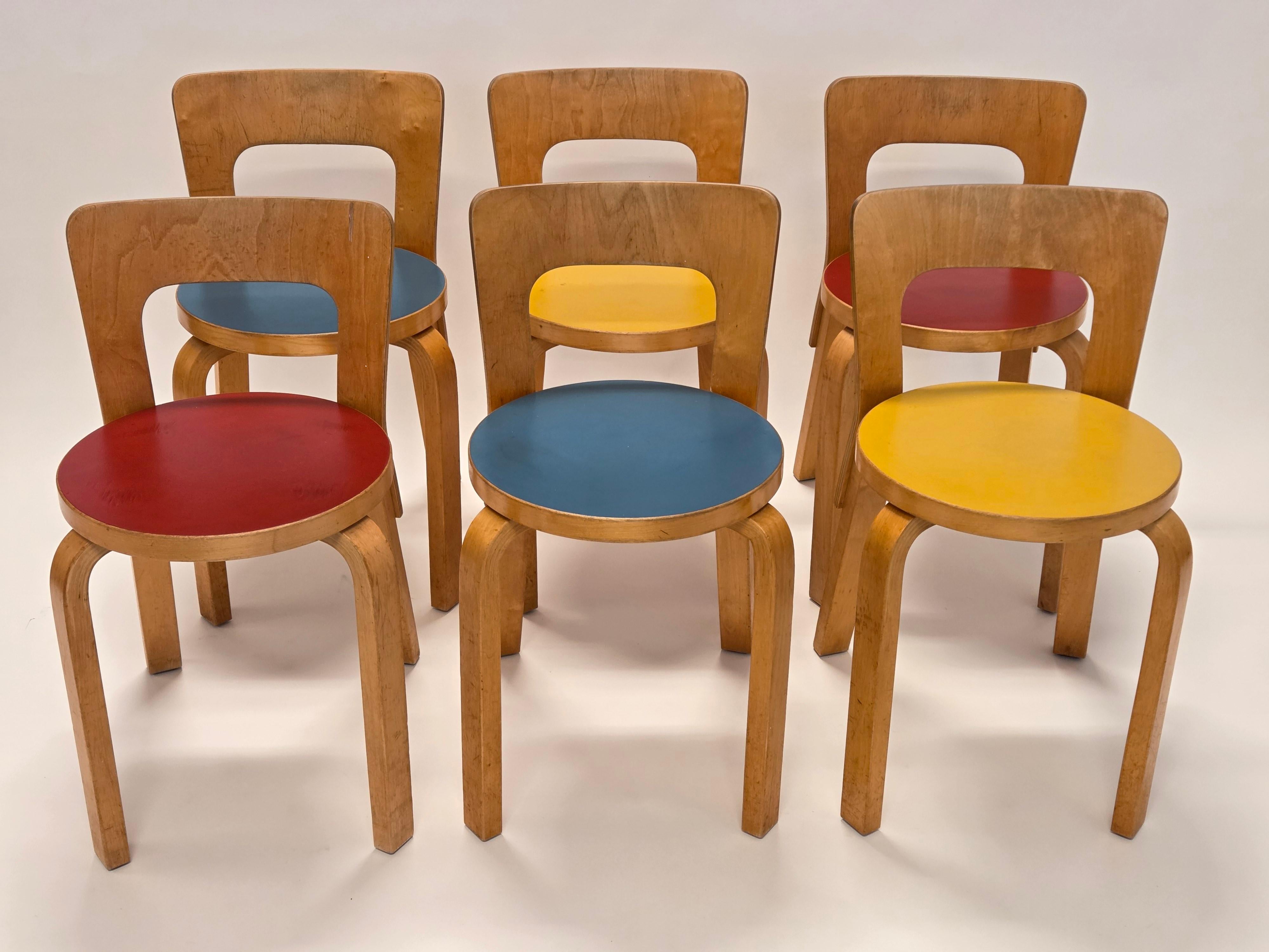 Table pliante Artek modèle DL82 et six chaises modèle 65, conçues par Alvar Aalto. La table a un beau plateau en linoléum bleu et les chaises ont des plateaux en linoléum bleu, jaune et rouge, deux chaises de chaque couleur. L'ensemble date