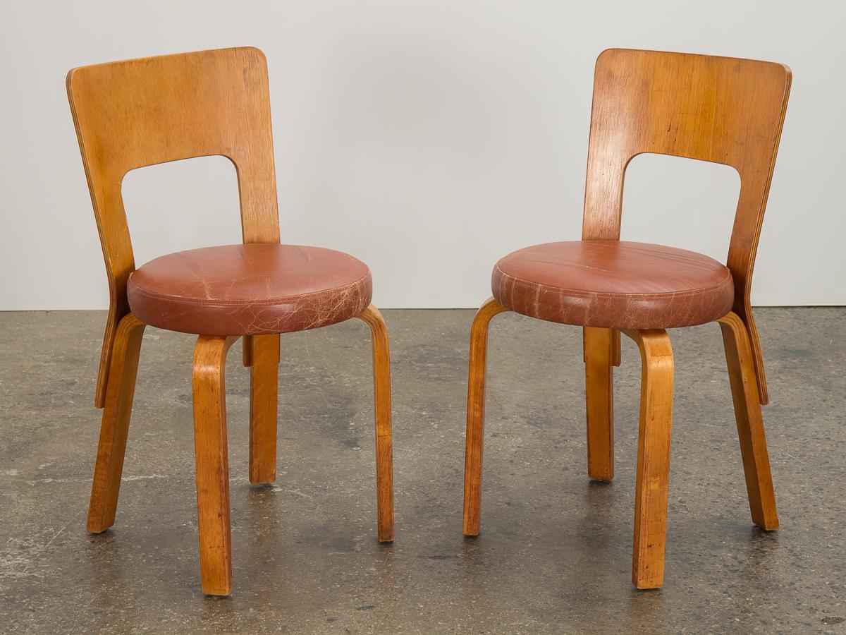 Early Model 66 dining chairs with leather seats, designed by Alvar Aalto for Finmar. Modern, graceful form designed in 1935. Stylish and functional chairs, supported by his signature steam-bent L-shape legs. Lacquered natural birch plywood exhibits