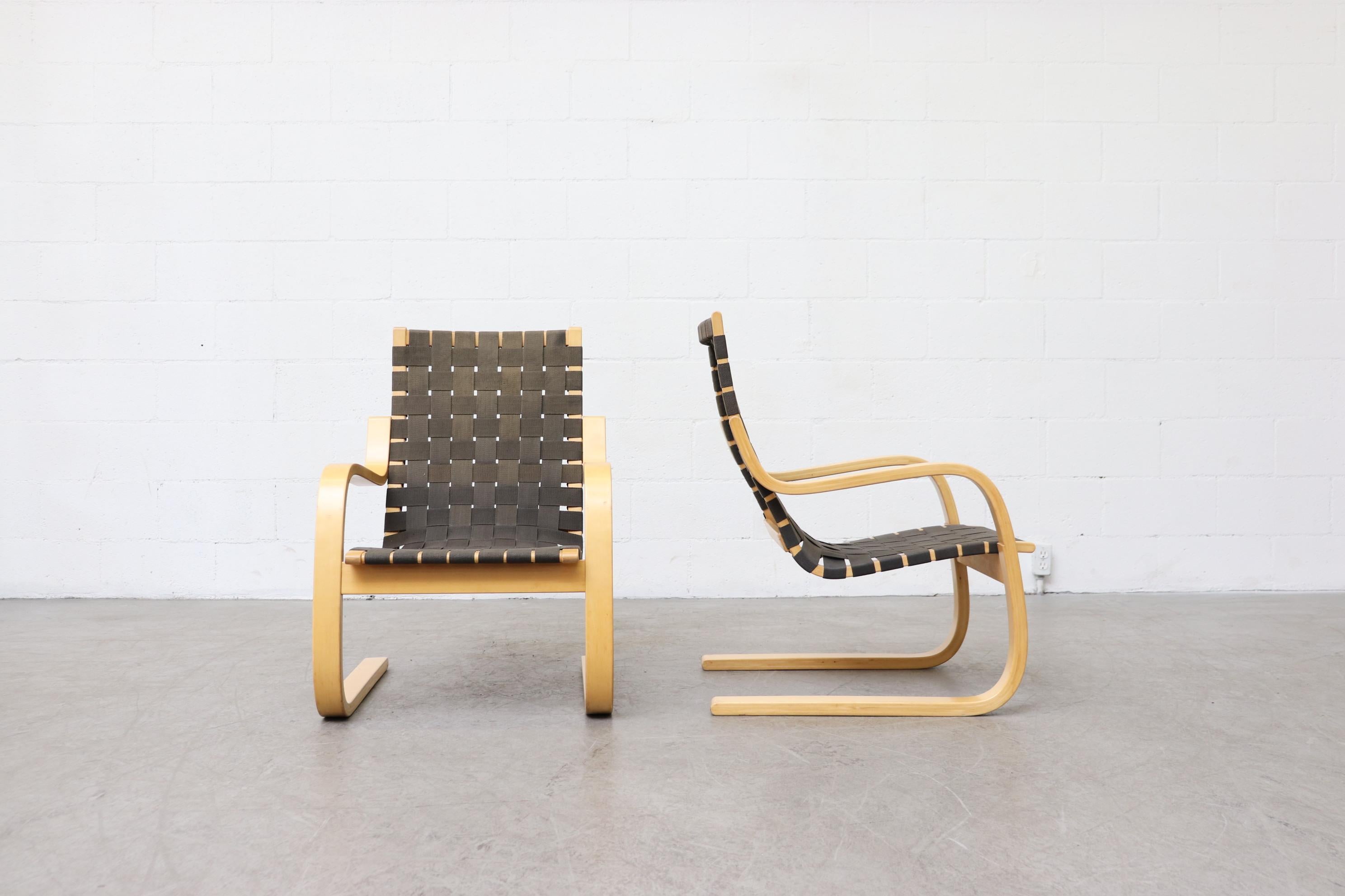 Alvar Aalto model 406 lounge chairs. Bent natural wood frames with woven canvas strapped seating. In original condition with some fading to the strapping. Fading and condition vary per chair, but are consistently aged. Priced individually.