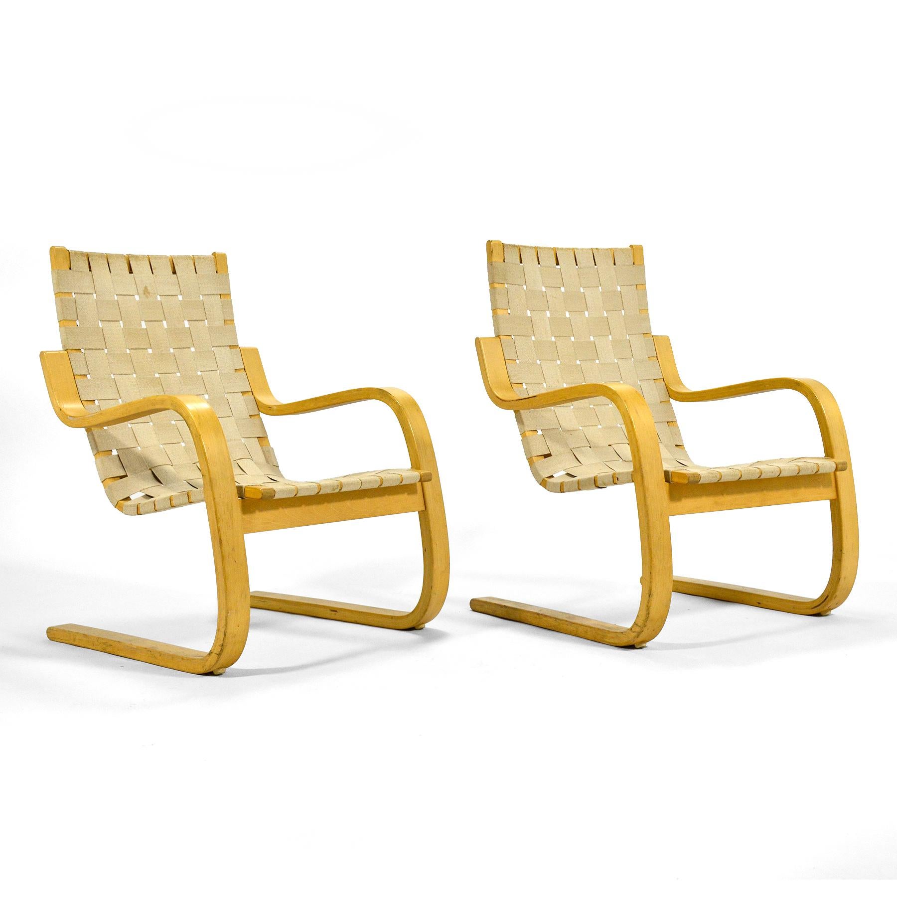 Aalto's 1936 design, the model 406 lounge chair is a perfect example of understated Finnish design. The bent wood cantelivered frame of laminated birch and natural cotton webbing supports the sitter in comfort. This pair of vintage chairs have a