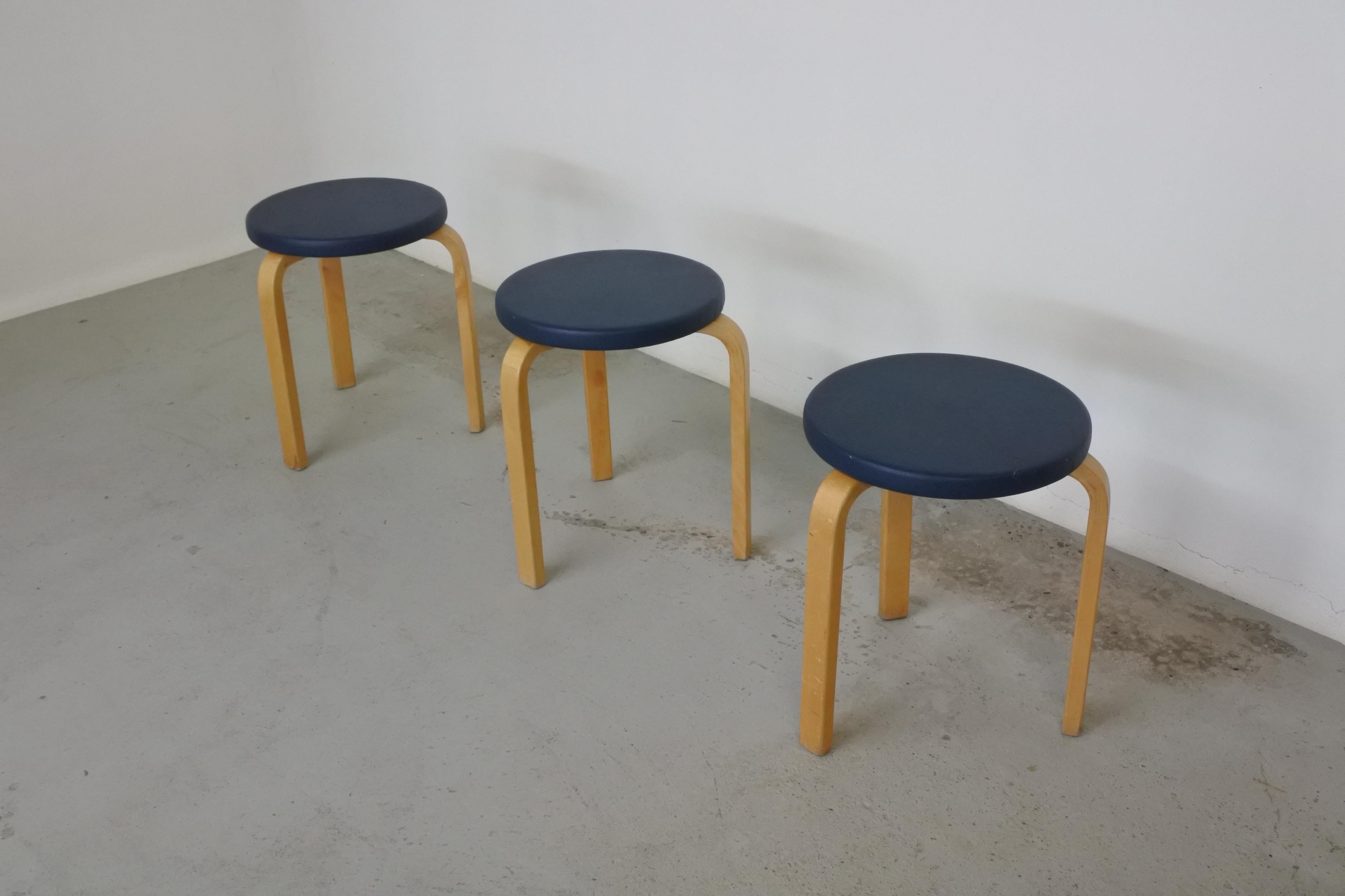 Set of 3 early tripod stools by Alvar Aalto.
Model 60.
Wood and upholstered seat in blue faux leather.
Made in Finland circa 1950.

Each stool bears the coat of arms of the city of Helsinki.

Good original condition, the faux leather shows