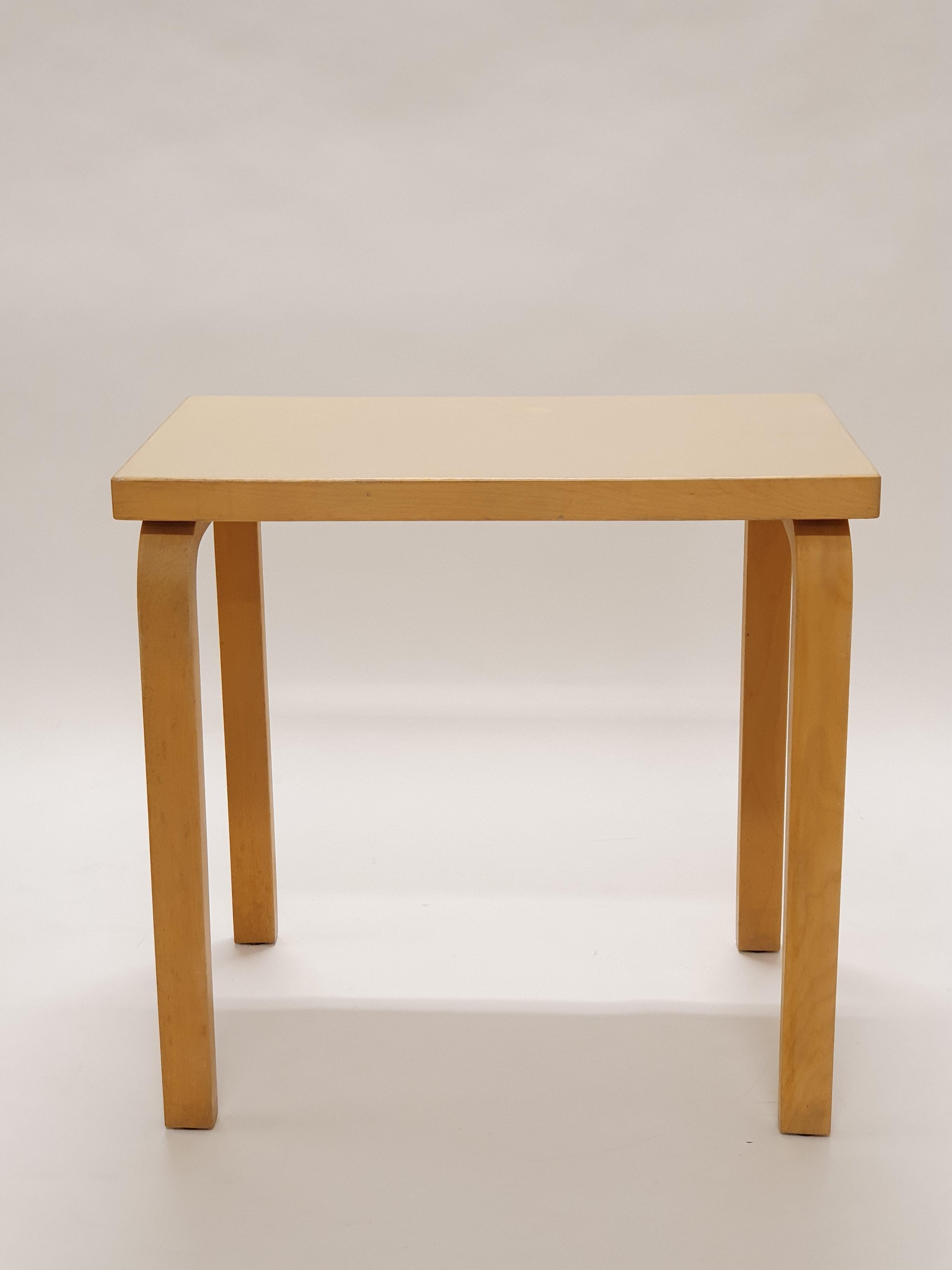 L-legged side table from 1950s designed by Alvar Aalto and manufactured by Artek. The table has beautiful patina of age and original cream white linoleum top. The table is in great condition.