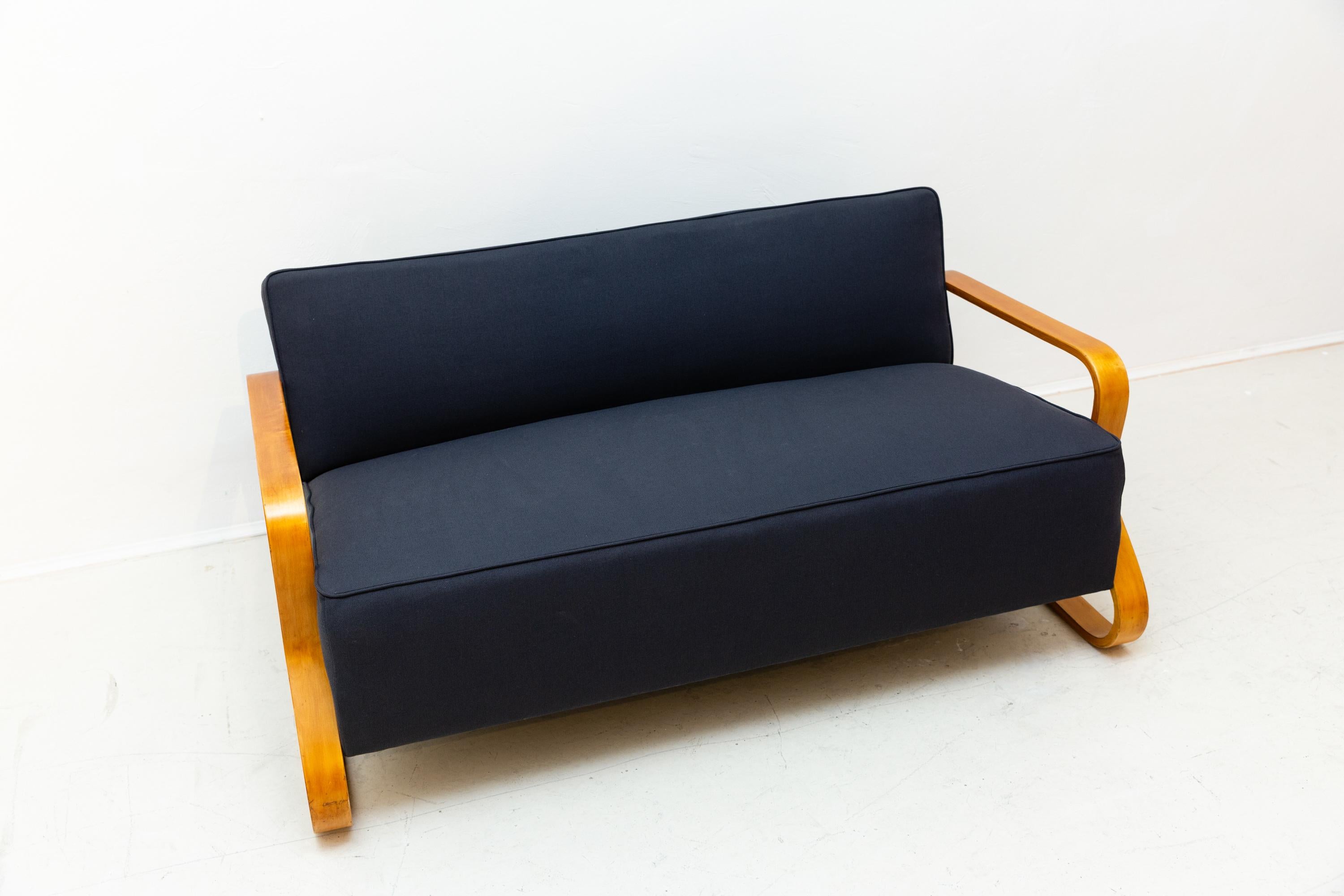 Alvar Aalto (1898-1976), 2-seat sofa model 44, designed 1931/32, manufactured by Finmar. . Wooden frame construction with lacquered birch side panels, vintage spring upholstery, newly textile recovered, dark blue fabric cover. In a very good