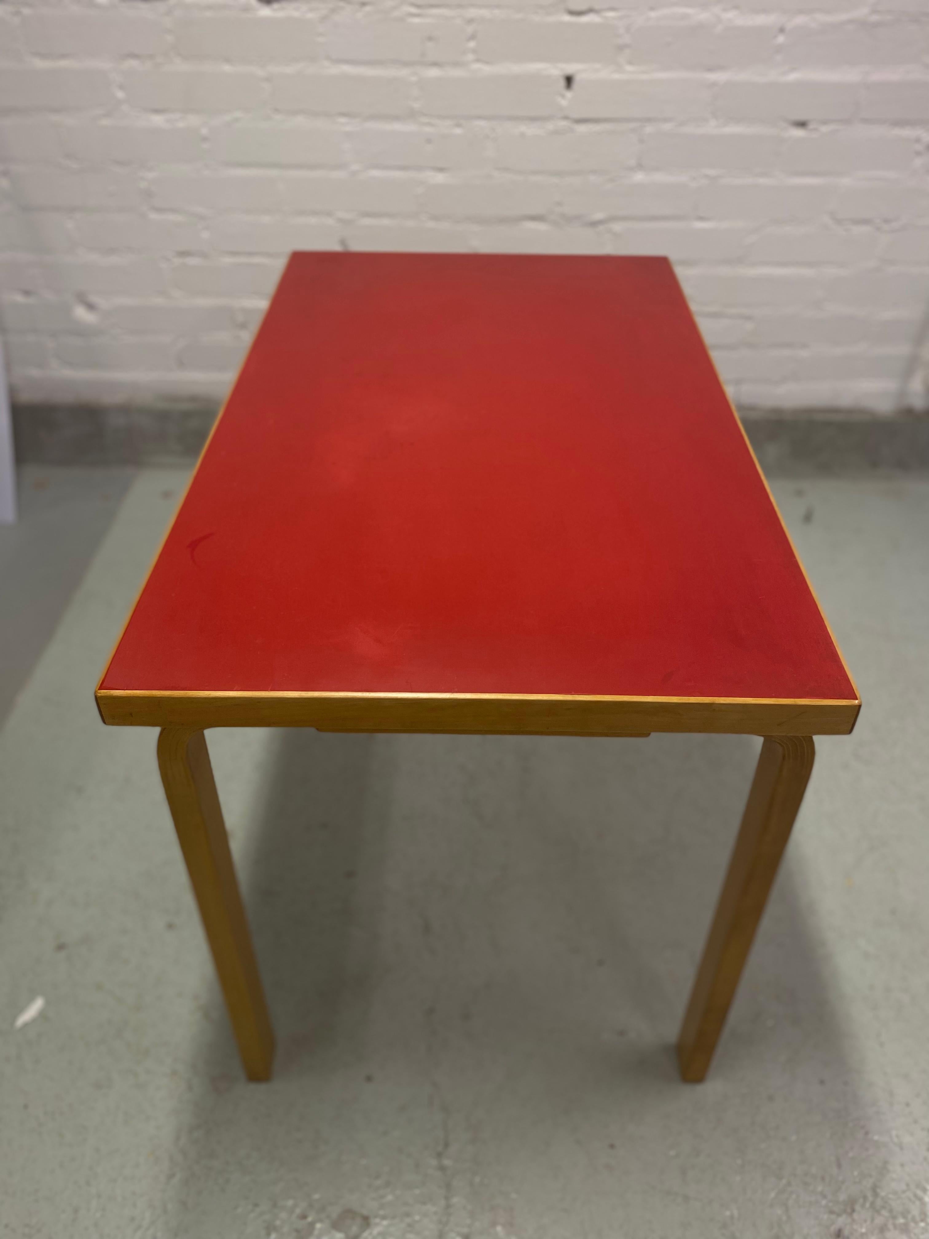 Alvar Aalto rectangular L-leg table in red linoleum top, manufactured by Oy Huonekalu-ja Rakennustyötehdas Ab and retailed by Artek since the 1930s. 

Alvar Aalto designs are famous worldwide for a number of reasons. Beauty and functionality are at