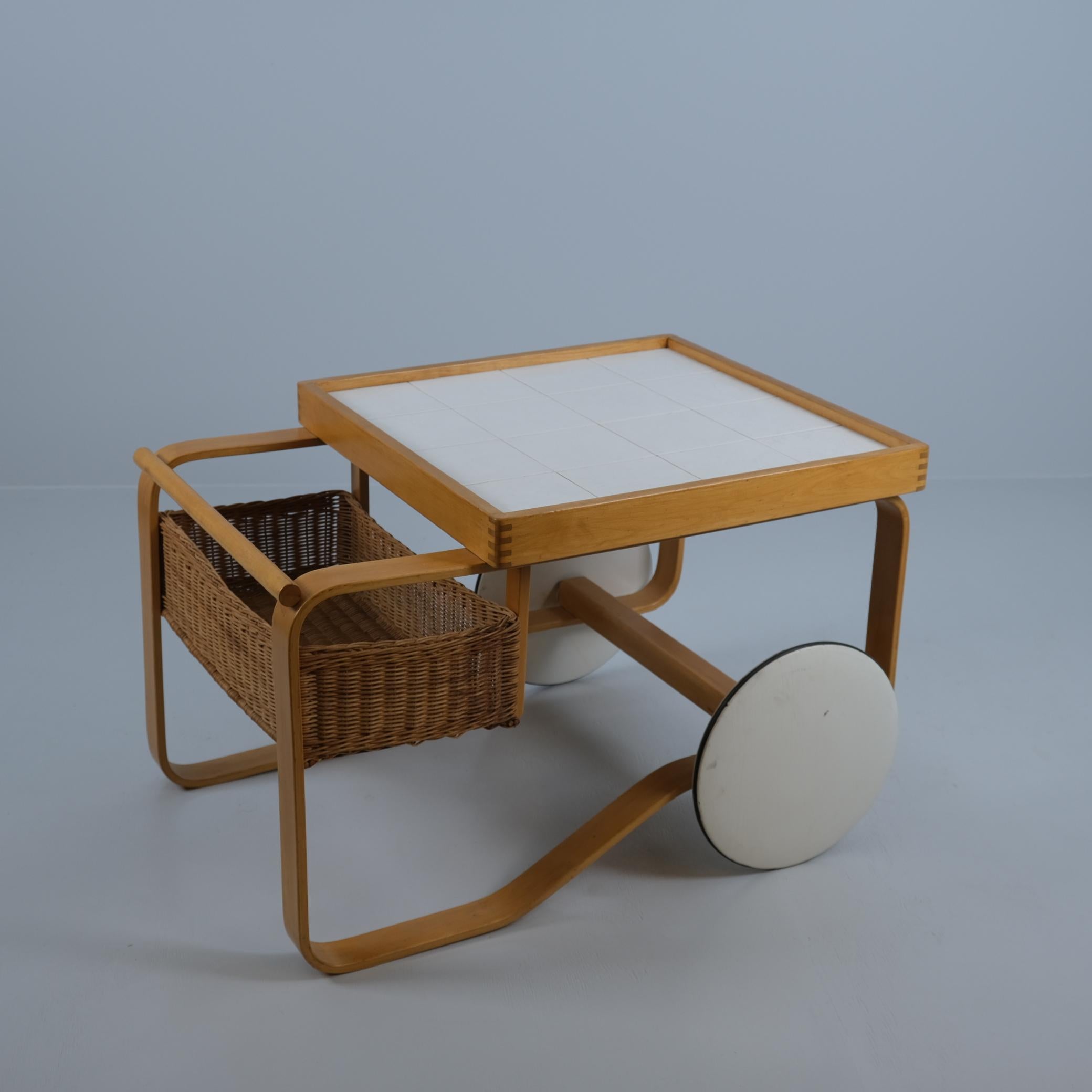 Eines der kultigsten und begehrtesten Stücke von Alvar Aalto. Dieser traditionelle, elegante und pragmatische Teewagen ist im Stil des modernen skandinavischen Designs gehalten. Der Wagen ist mit Keramikfliesen und einem Rattankorb ausgestattet und