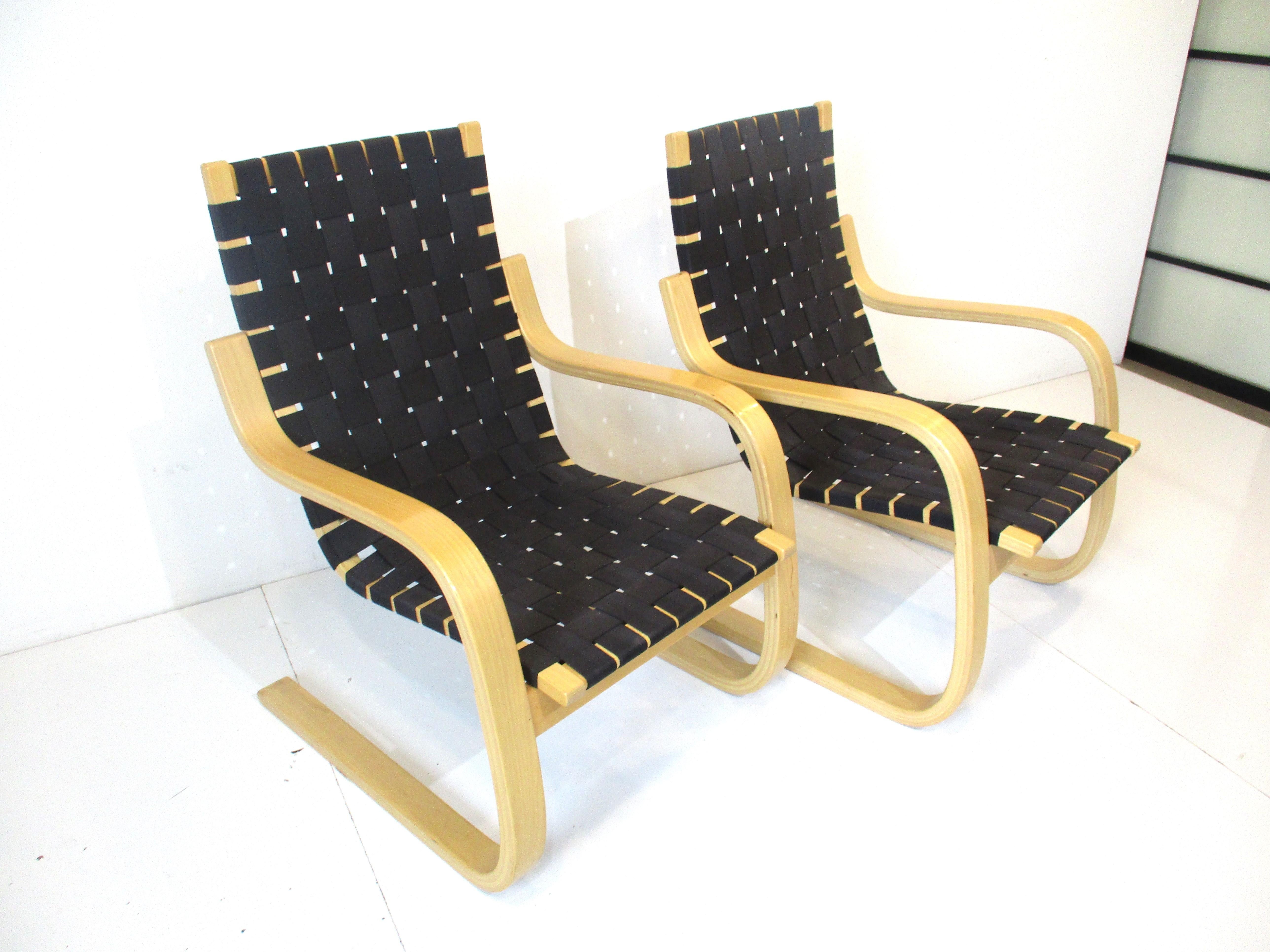 A pair of sculptural bent birch wood framed lounge chairs with black woven strap seating by Finish designer Alvar Alto. A very comfortable Classic form with ergonomics in mind, retains the label from the importer ICF manufactured in Finland by Artek