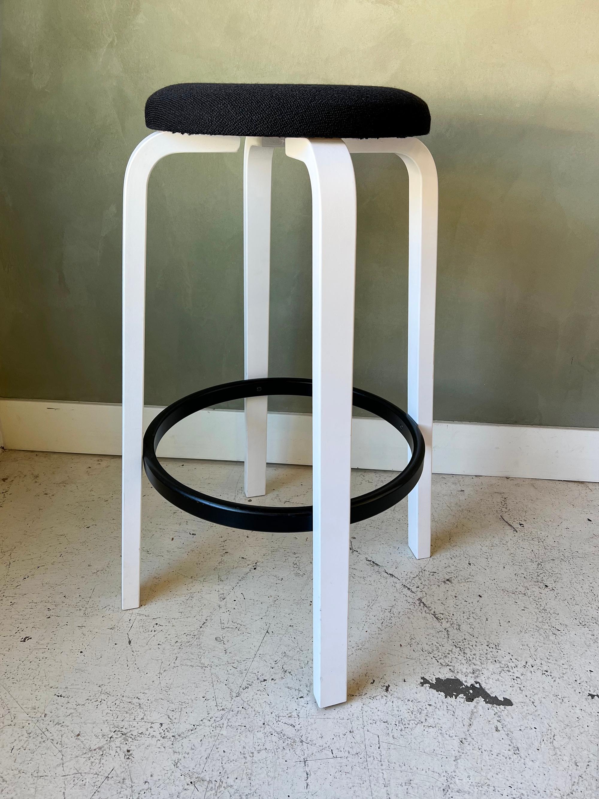Newer production bar stool by Alvar Aalto for Artek. Custom color scheme with white legs, black footrest, and black upholstery. Upholstery is clean and some have small chips in the paint but are overall in like-new condition.