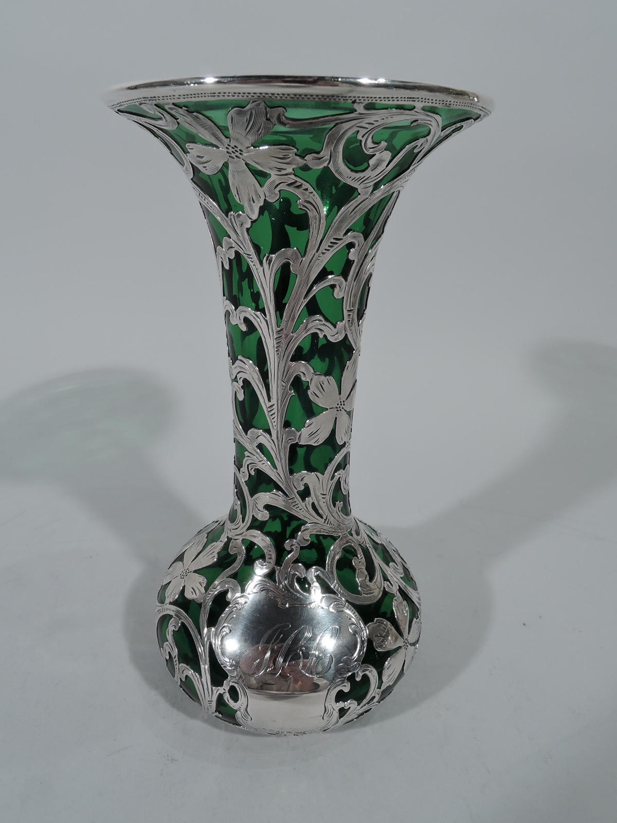 Art Nouveau emerald glass vase with engraved silver overlay. Made by Alvin in Providence. Bellied bowl with cylindrical neck and flared rim. Foliate scroll pattern interspersed with flowers. Asymmetrical cartouche engraved with script monogram.