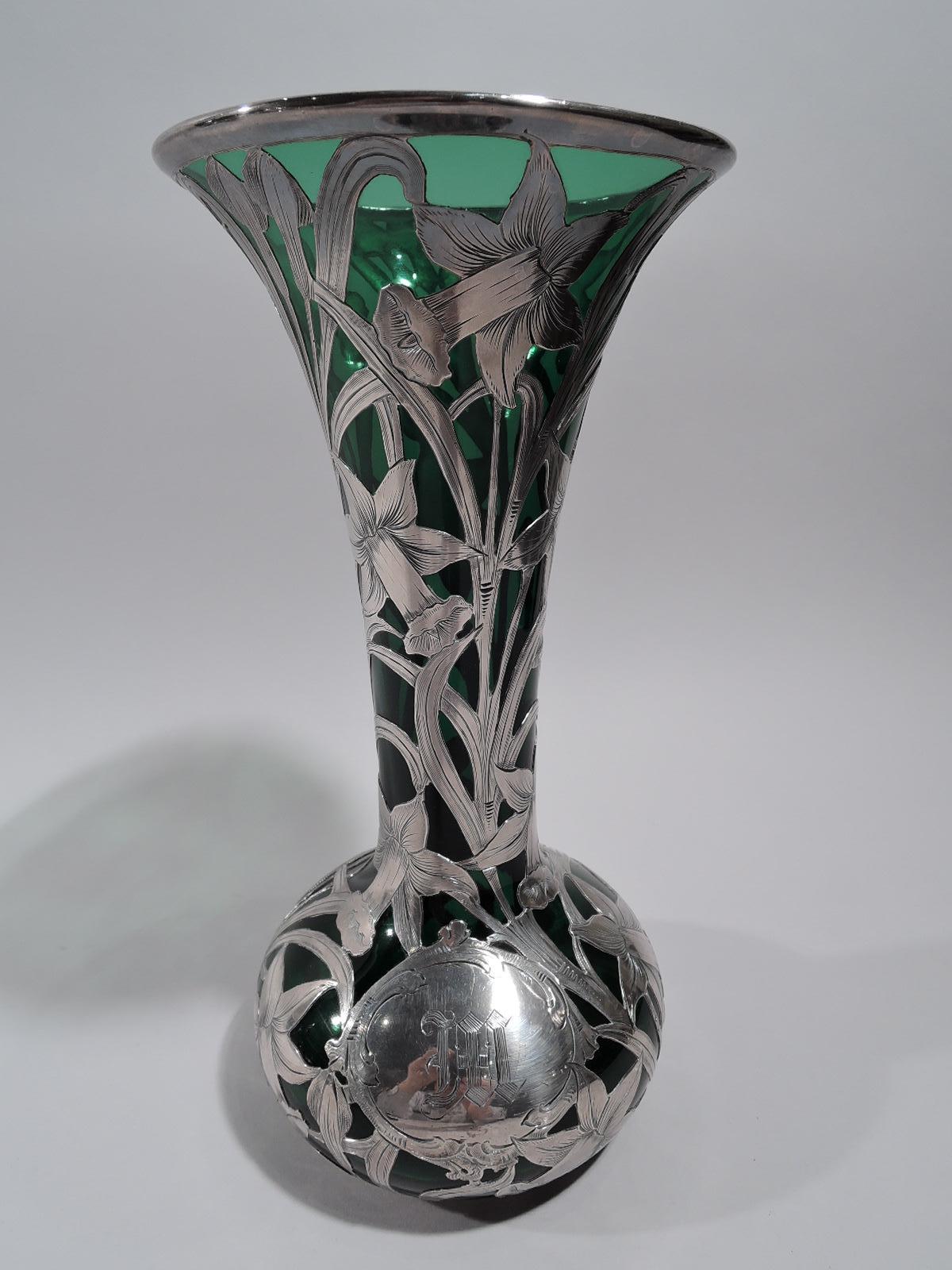 Turn-of-the-century Art Nouveau green glass vase with engraved silver floral overlay. Conical mouth and neck, and bellied bowl. Overlay in form of daffodils with entwined and overlapping flower heads and stems. A pretty example of putting the