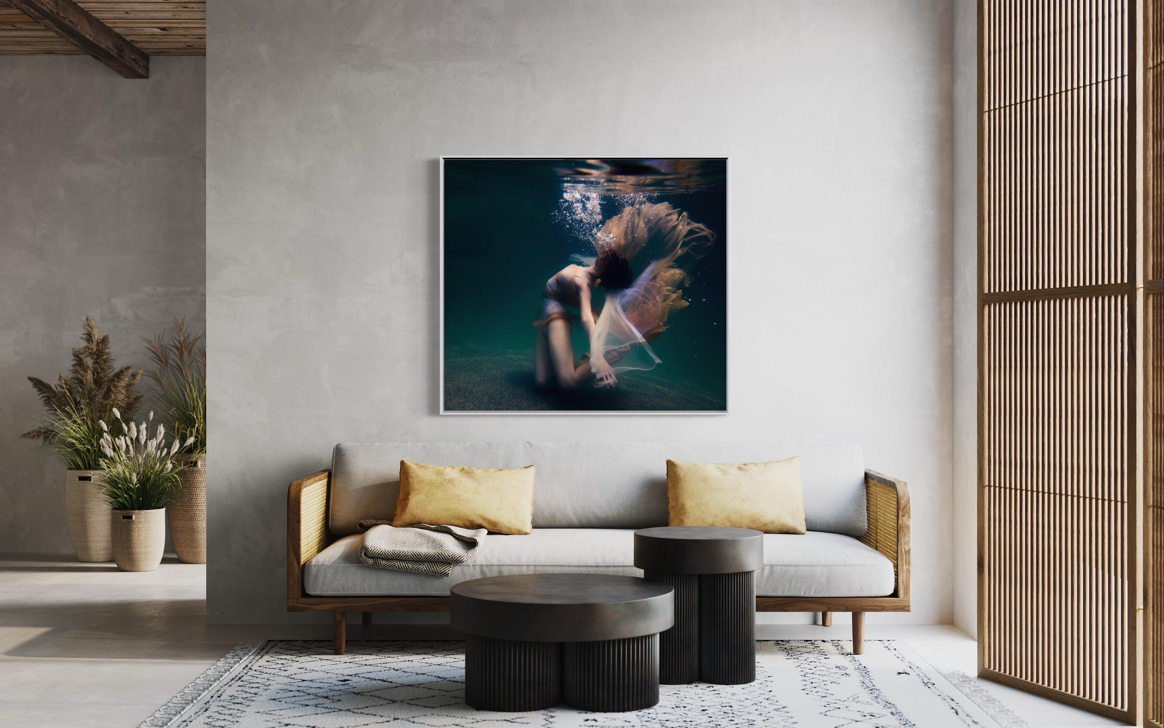 This abstract figural limited edition fine art photograph by Alyssa Fortin captures the female form in a dancer-like pose, submerged in water. Bubbles reach toward the surface of the water as the figure exhales from beneath it, with soft fabric