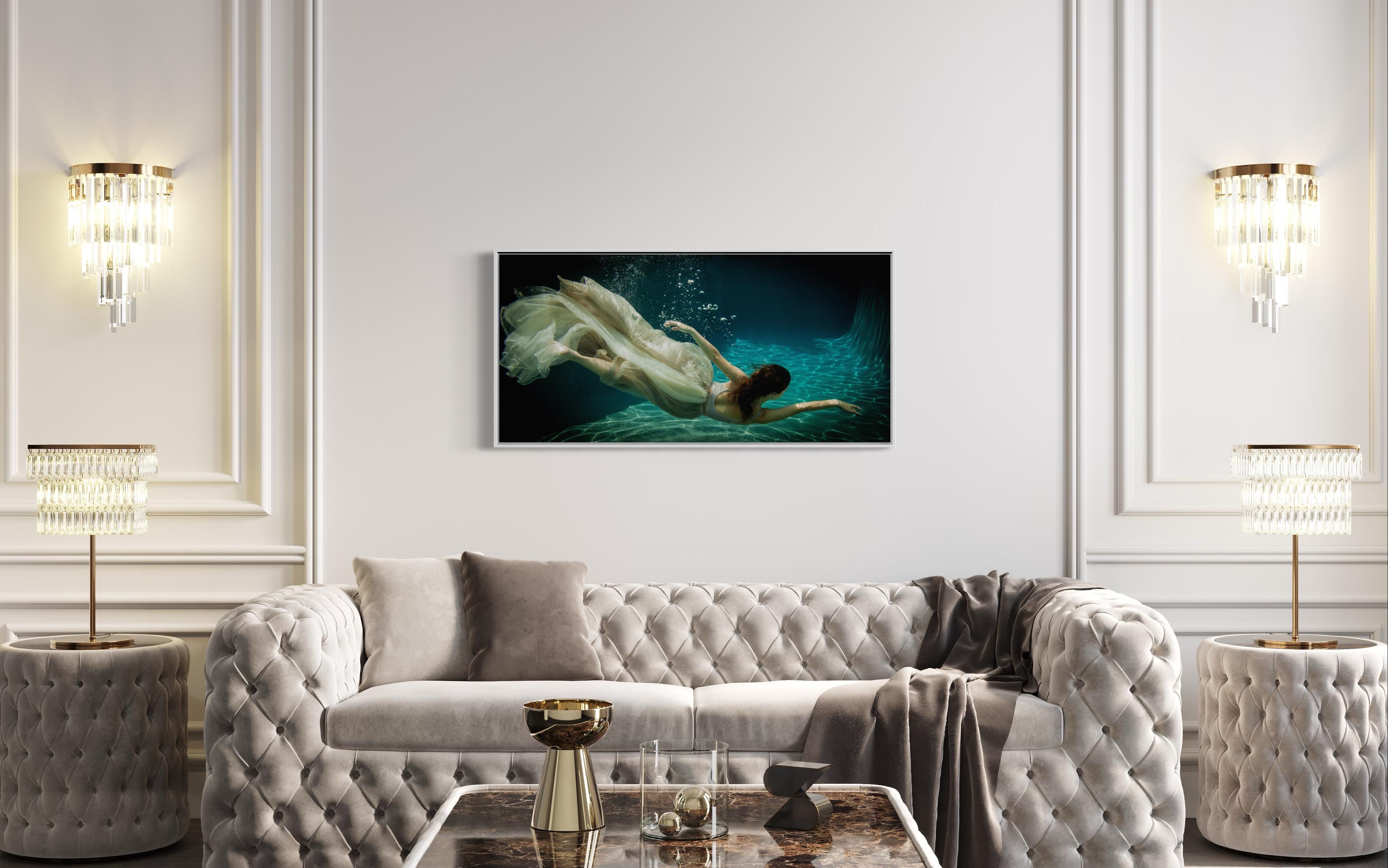 This contemporary figural limited edition photograph by Alyssa Fortin captures a female figure, wearing a dress made of light, soft fabric, swimming through water in an almost dancer-like fashion. The warm neutral tones of the figure and her dress