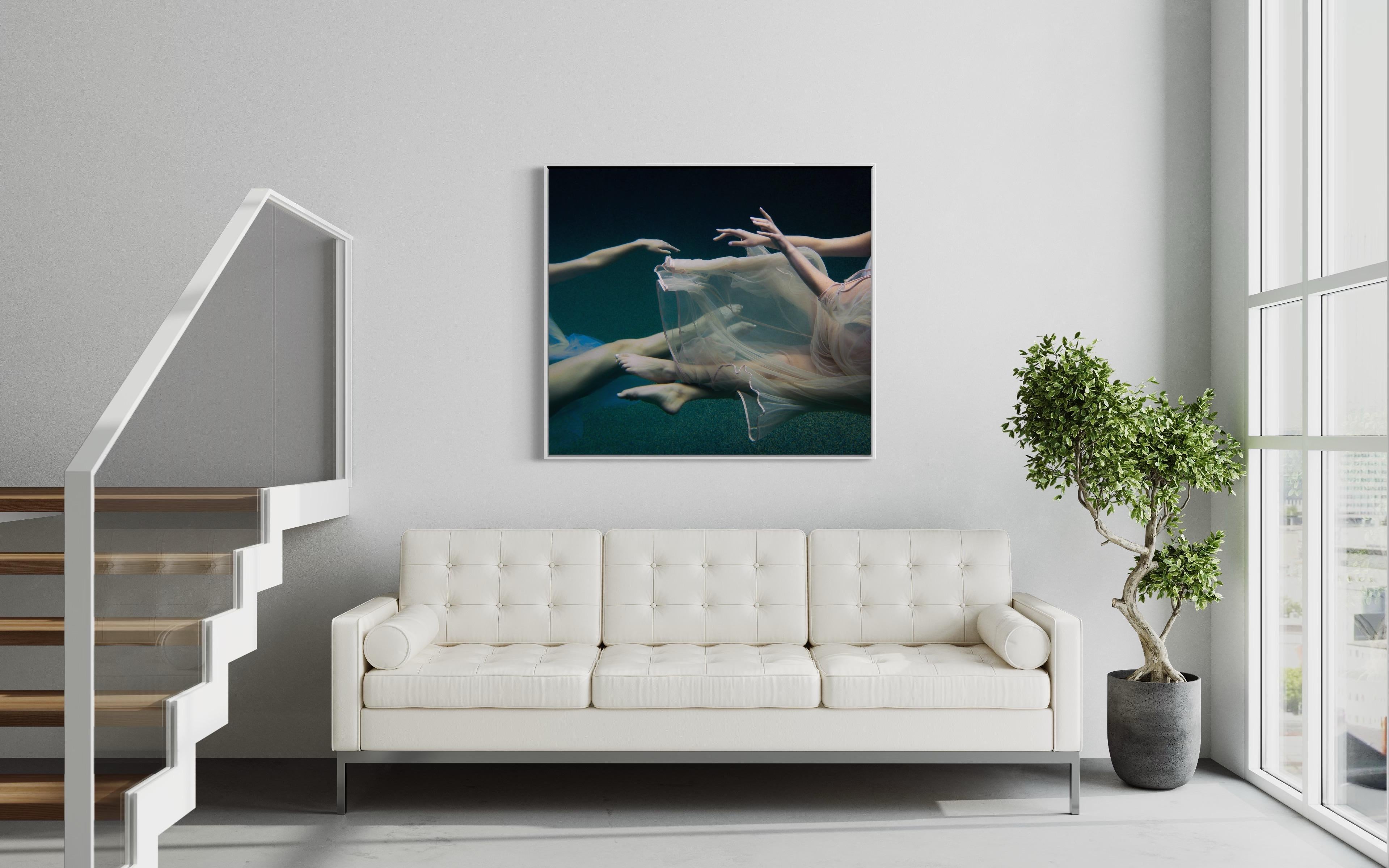 Cette photographie d'art en édition limitée d'Alyssa Fortin capture les bras et les jambes de formes féminines de chaque côté de la composition, enveloppées d'un tissu de tulle doux alors qu'elles sont immergées dans l'eau. Les sujets flottent sous