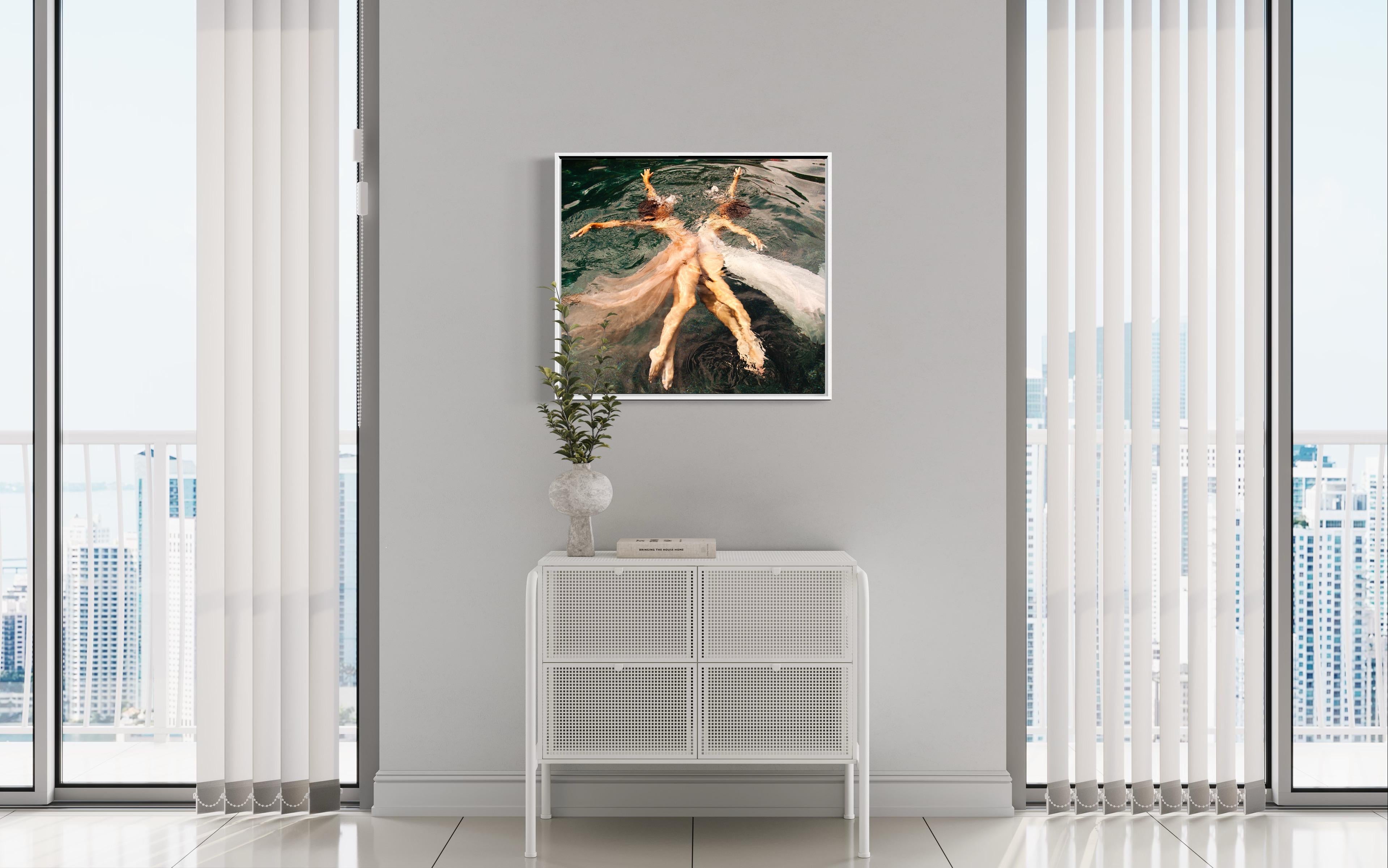 This contemporary figural limited edition photograph by Alyssa Fortin features a view from above the surface of water, with two female figures posed in dancer-like poses. Facing one another, they extend their arms and legs with blush and white