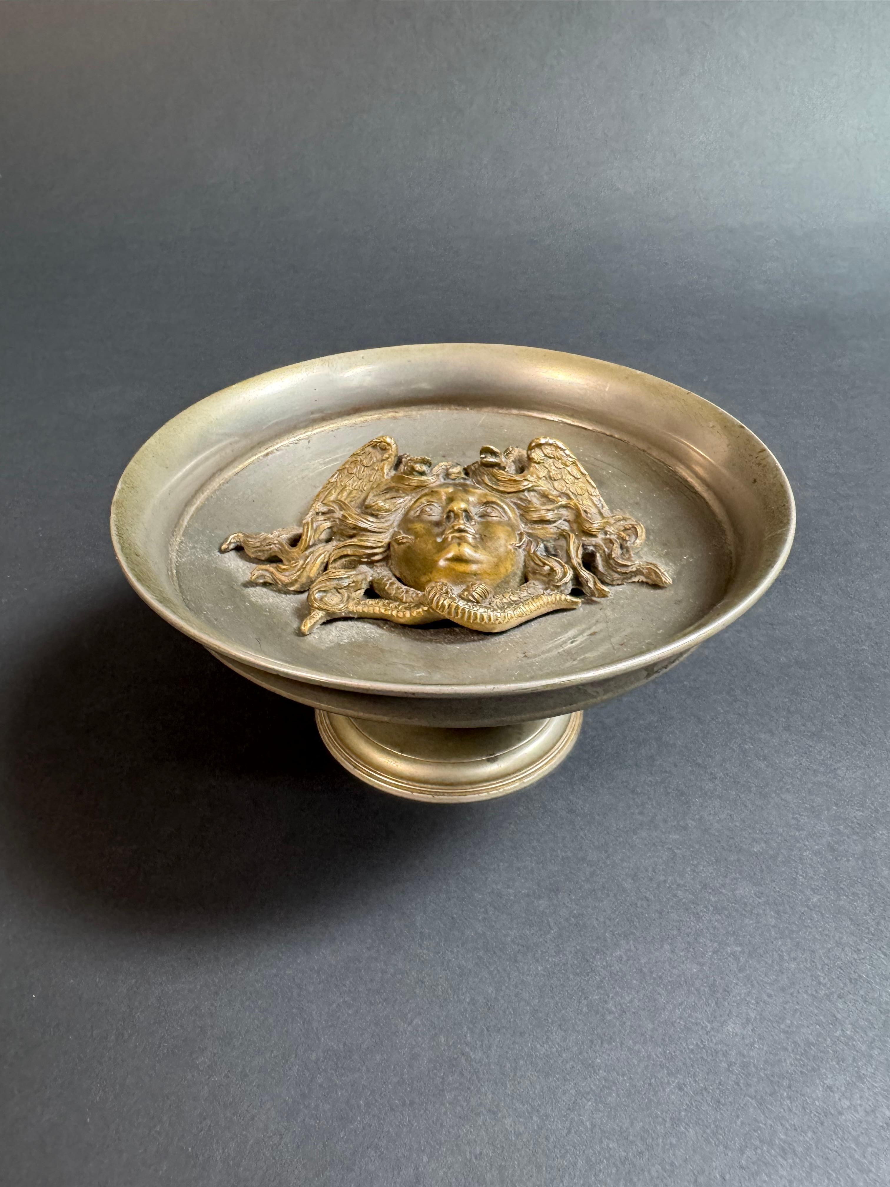 Alzatina decorativa di Vincenzo Gemito del XIX secolo.

L'alzatina è caratterizzata da un distintivo e dettagliato bassorilievo in bronzo della testa di Medusa, una delle tre Gorgoni della mitologia greca, i suoi capelli sono rappresentati come