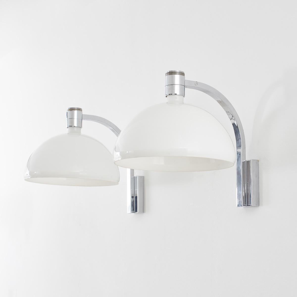 A pair of large wall lights with white glass shades mounted on chromed arms by Franco Albini, Franca Helg and Antonio Piva. This wall light is designed to allow for the glass shades to be mounted to light upwards or downwards.

The glass is in